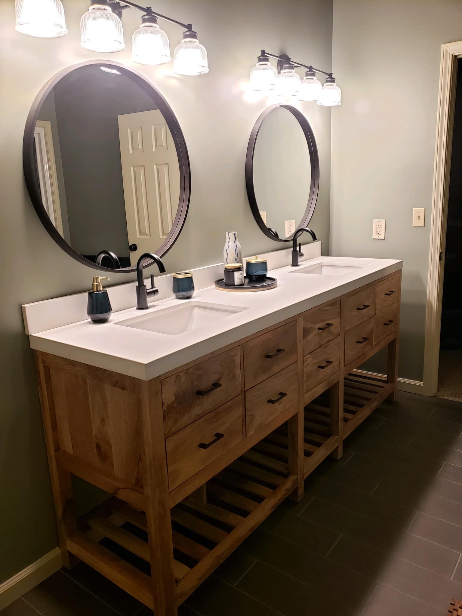 Bathroom with wood vanity, two sinks, round mirrors, and overhead lights.