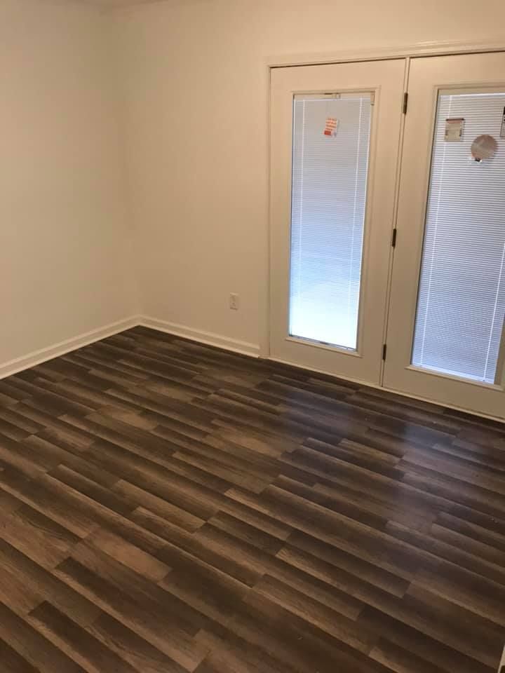Empty room with dark wood-look flooring, white walls, and French doors with blinds.