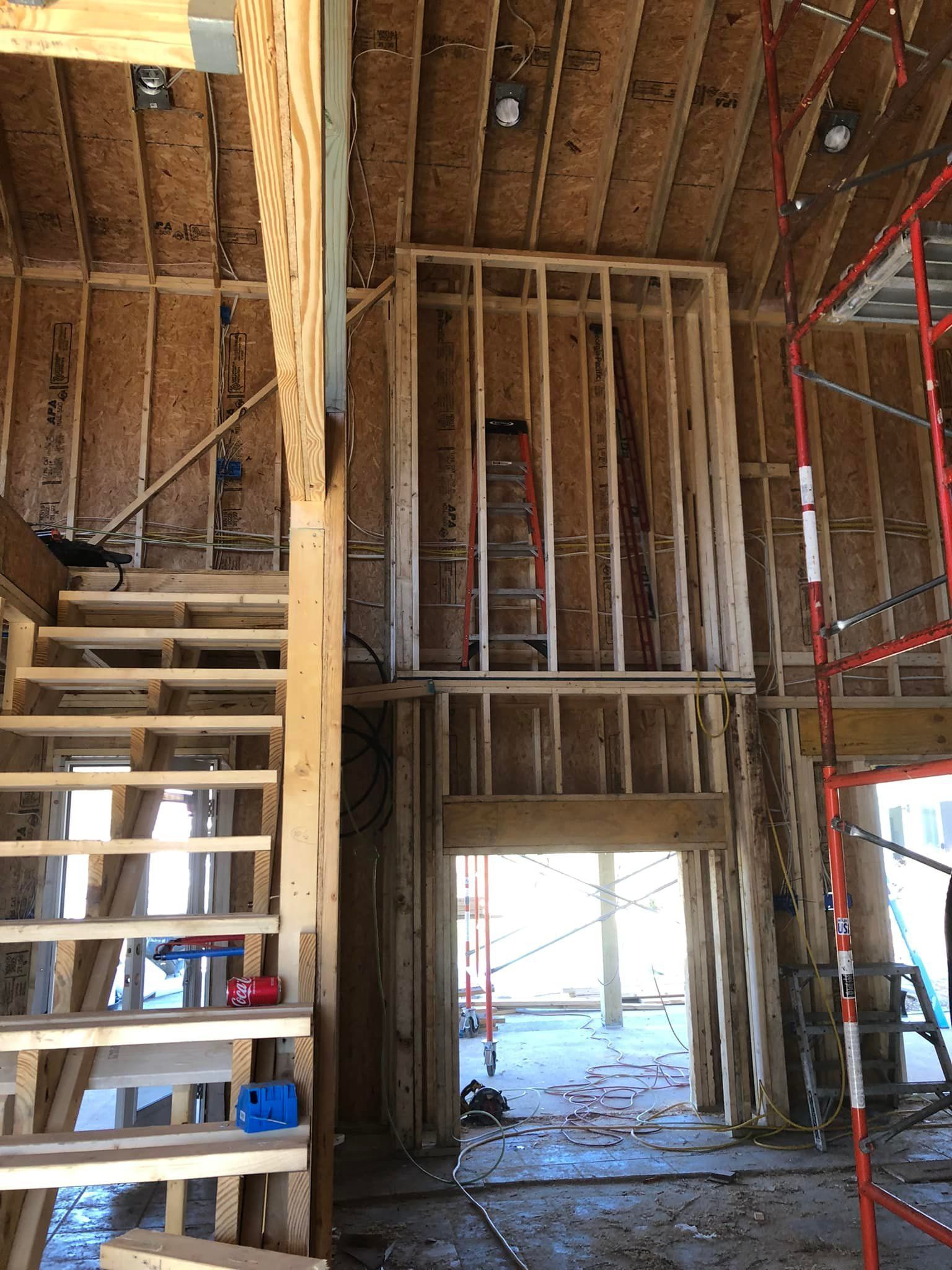 Interior of a house under construction; wooden frame stairs and wall with a doorway. Red scaffolding is on the right.