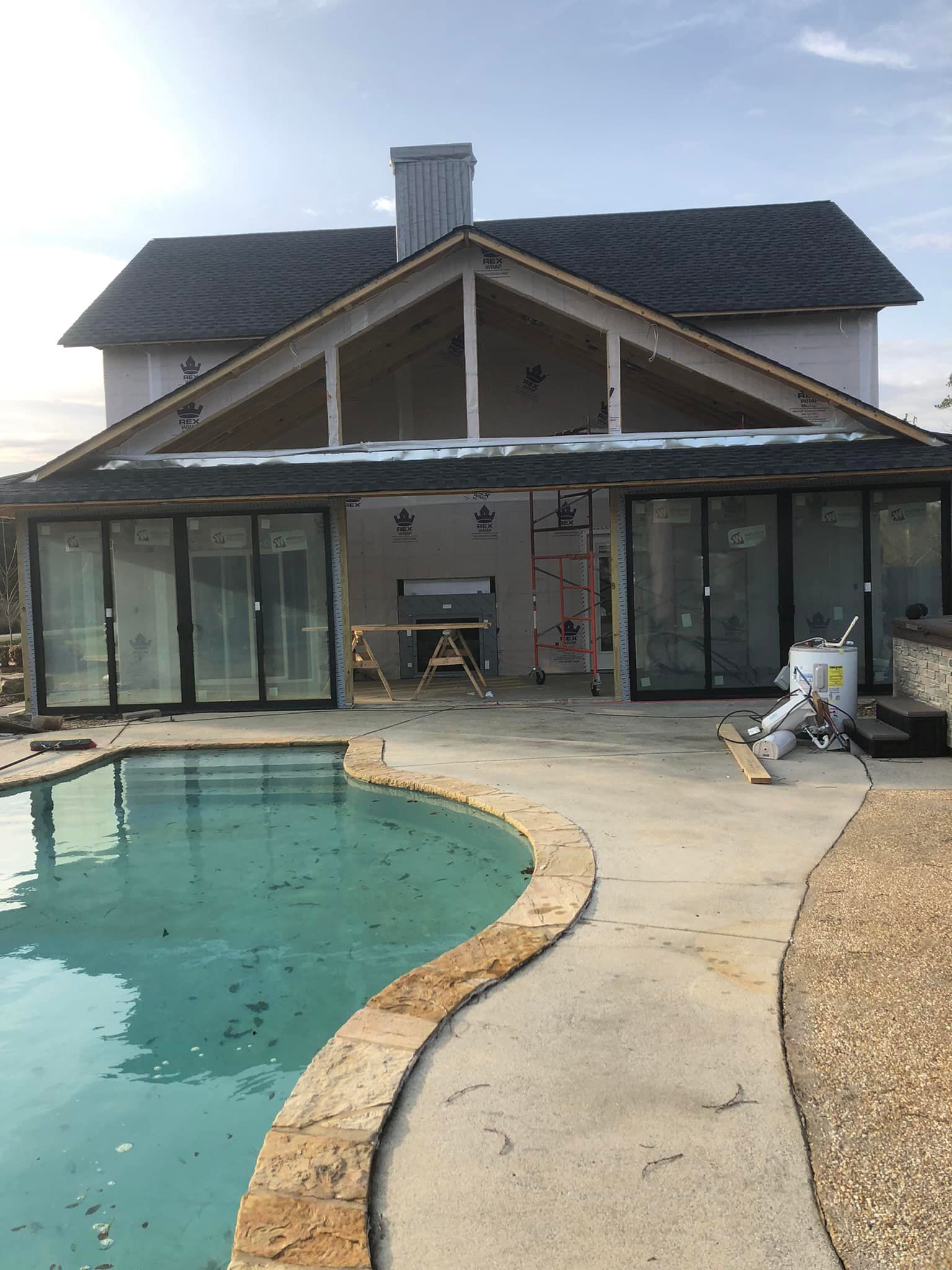 Backyard patio under construction with pool in the foreground and house in the background.