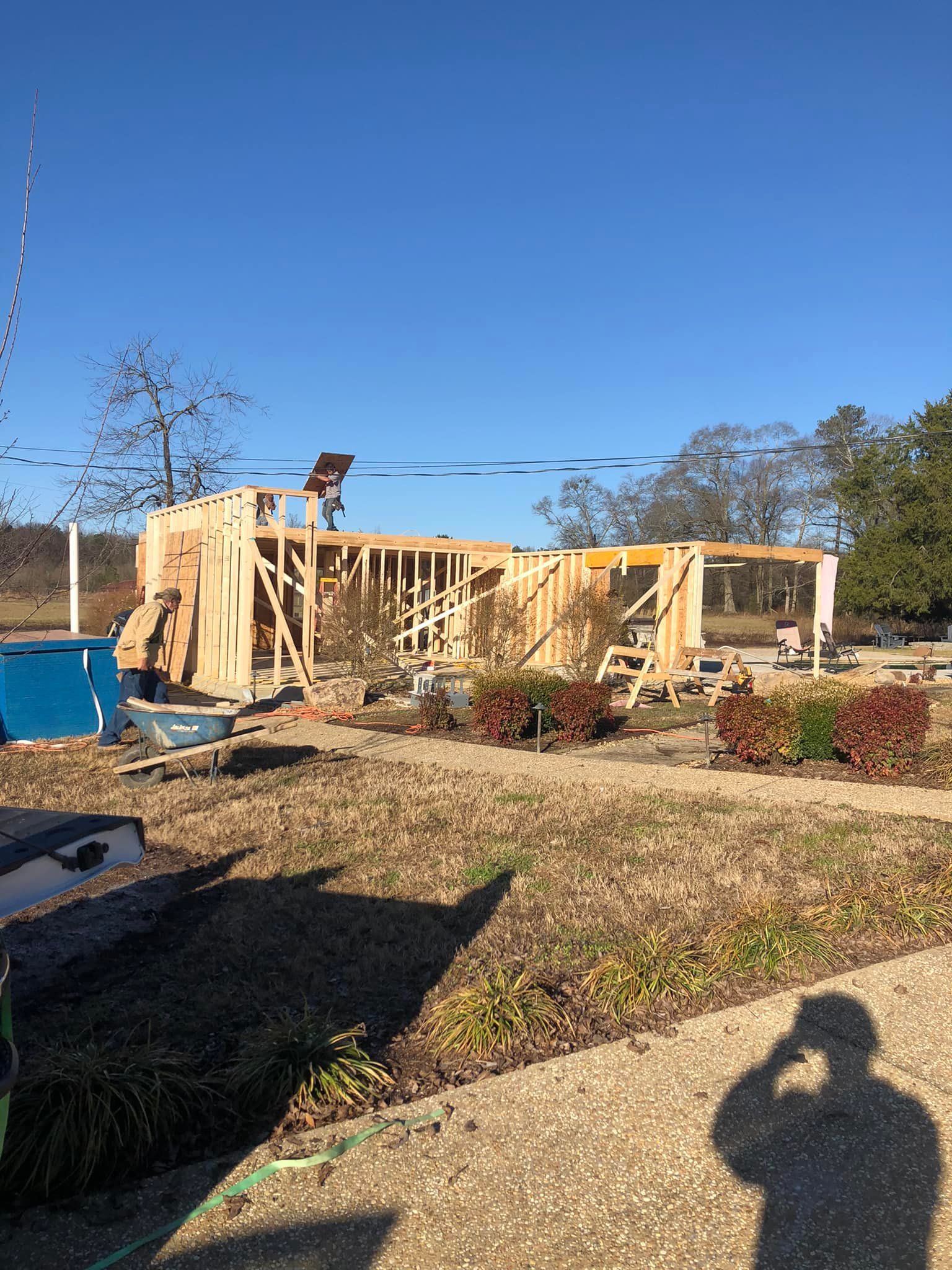 Construction site of a wooden house frame, with a worker on the roof under a clear blue sky.