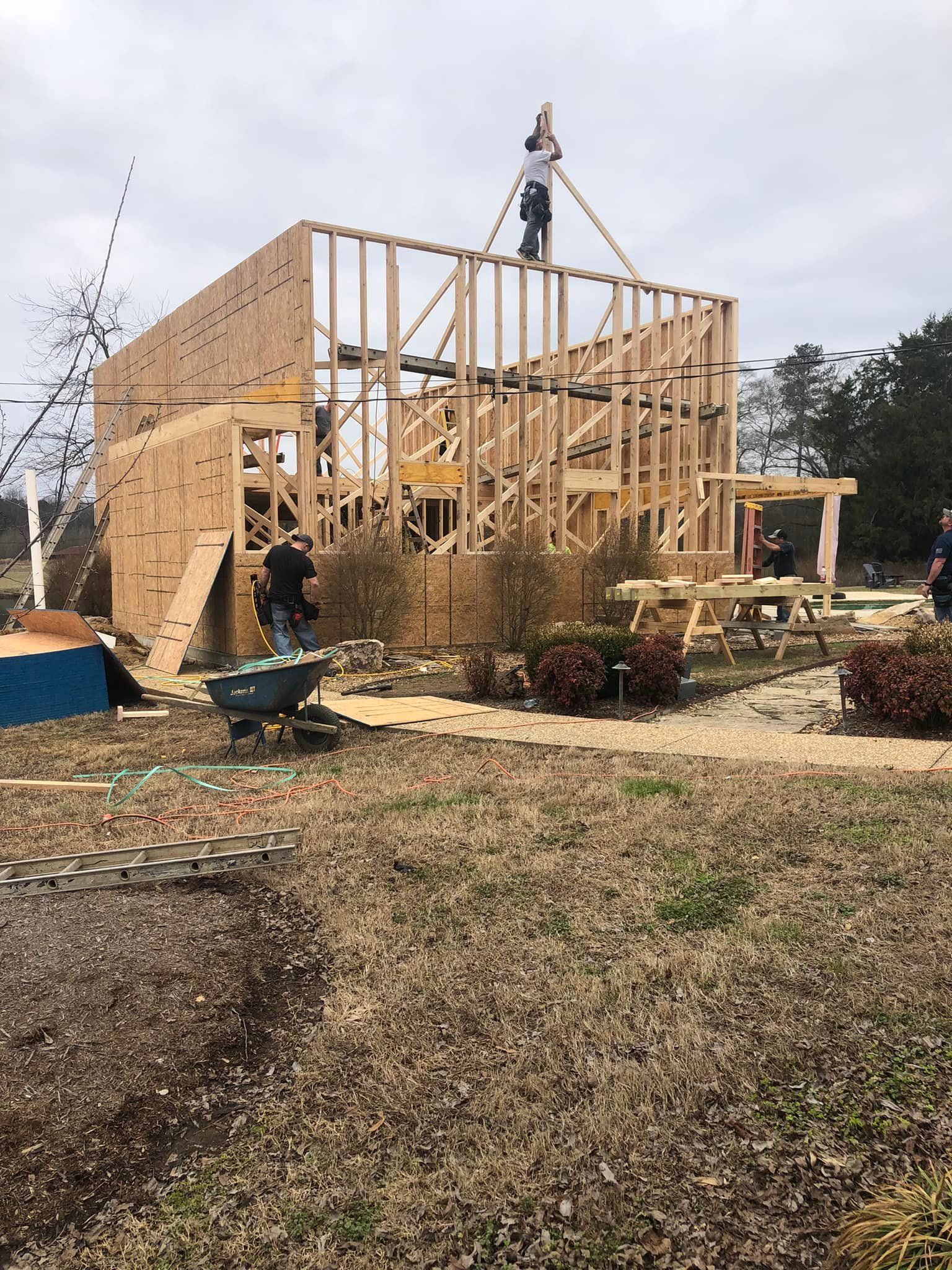 Construction workers building a wooden framed structure outdoors on a cloudy day.