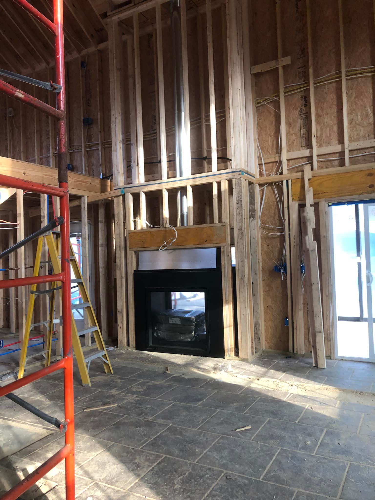 Interior of a building under construction, showing wooden framing around a fireplace and tall ceiling.