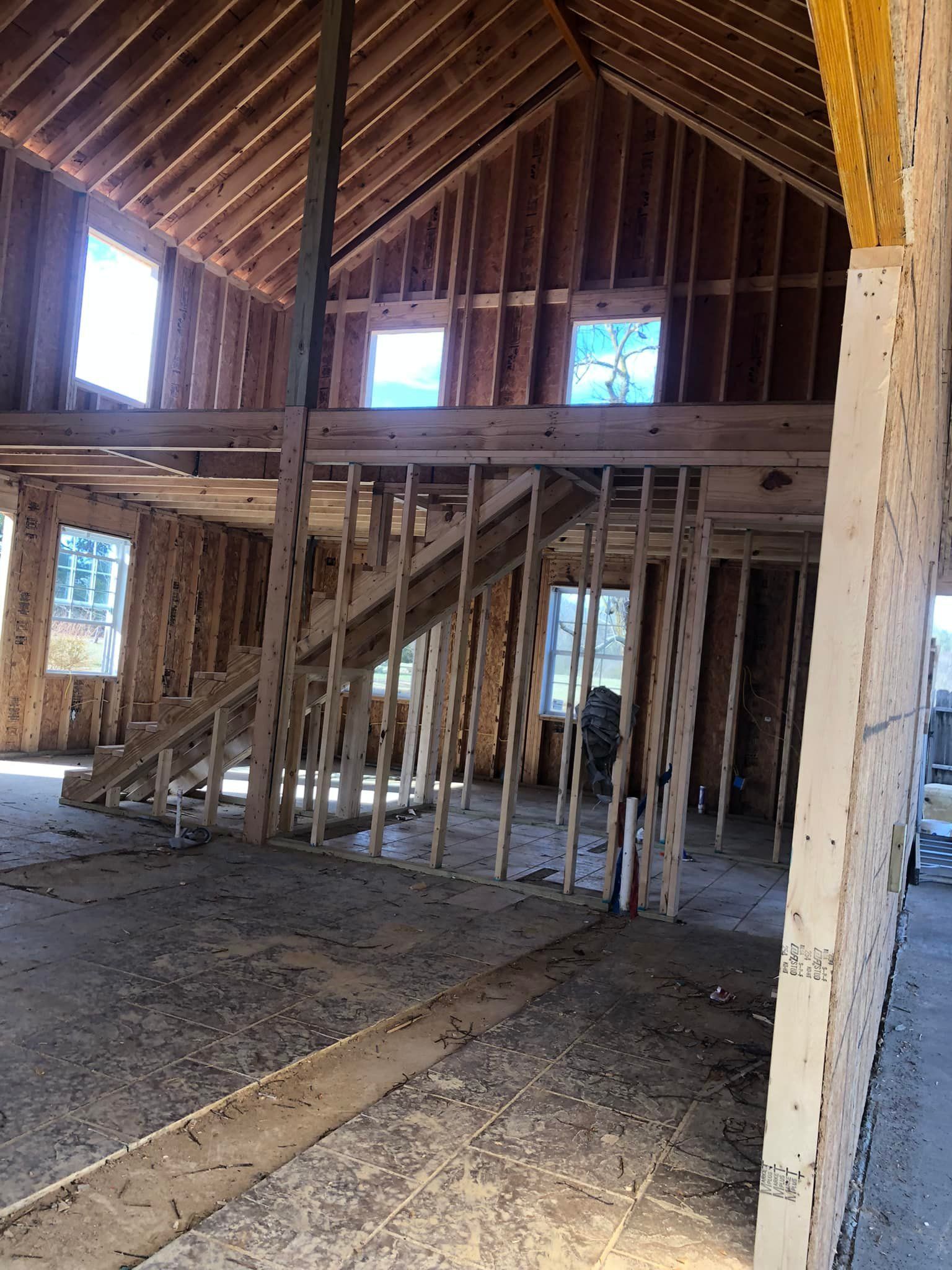Interior of a building under construction, showing wooden framing, a staircase, and windows.