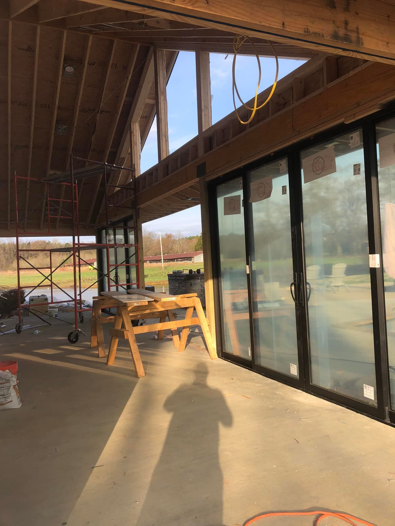 Construction site with partially built wooden roof and sliding glass doors. Shadow of person on concrete floor.