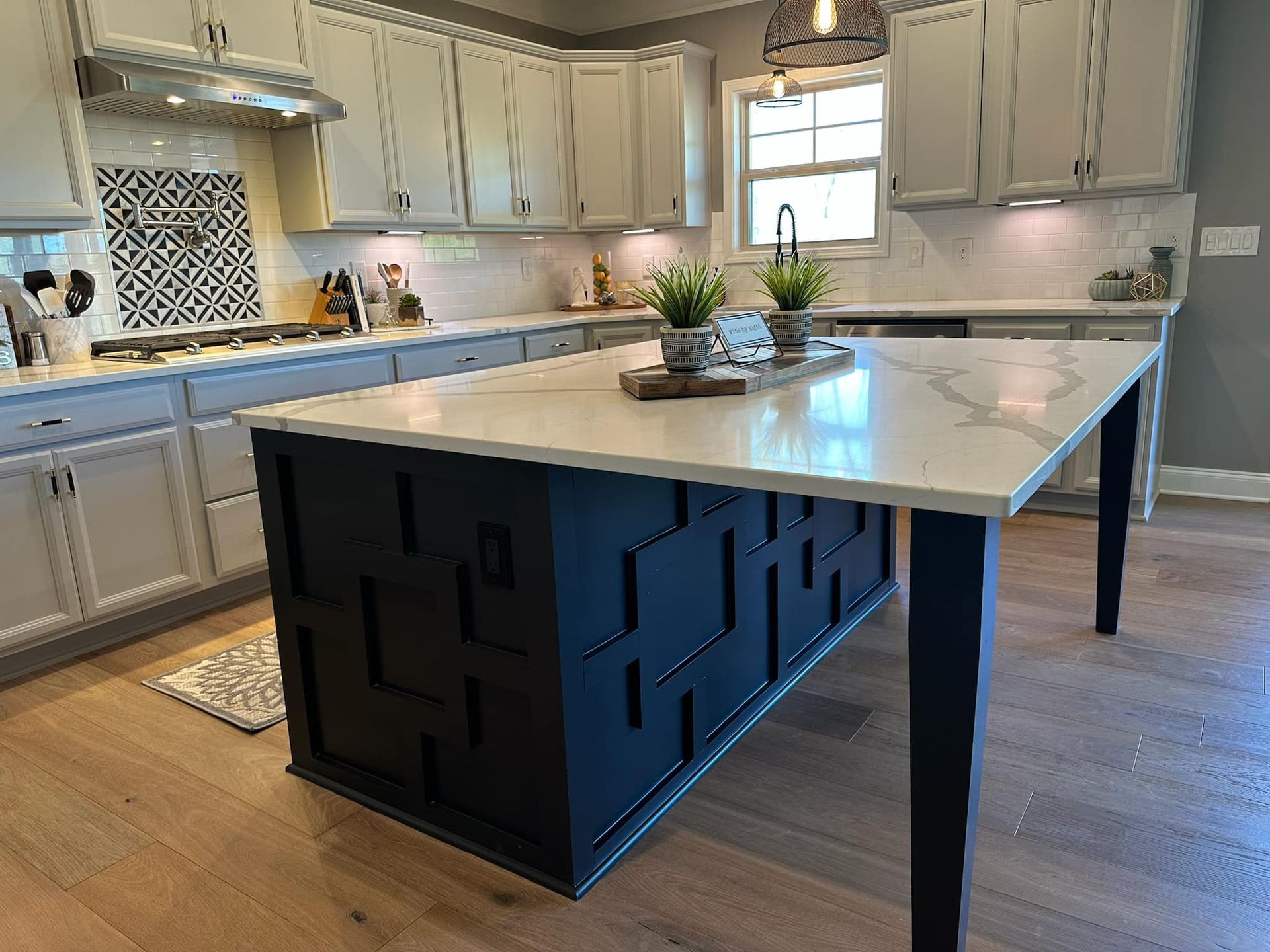 Kitchen with white cabinets, dark blue island with white countertop, and light wood floor.