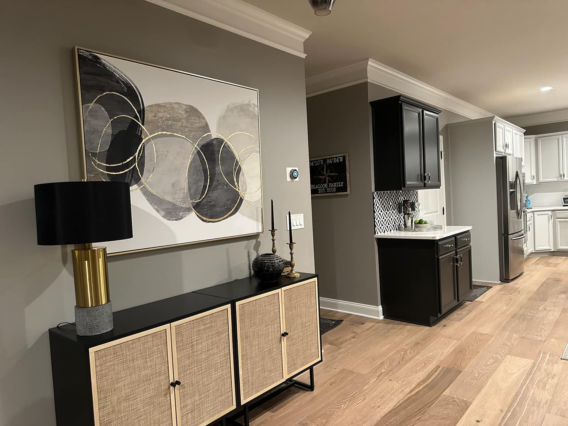 A modern living space with a black and gold console table, abstract art, and access to the kitchen.