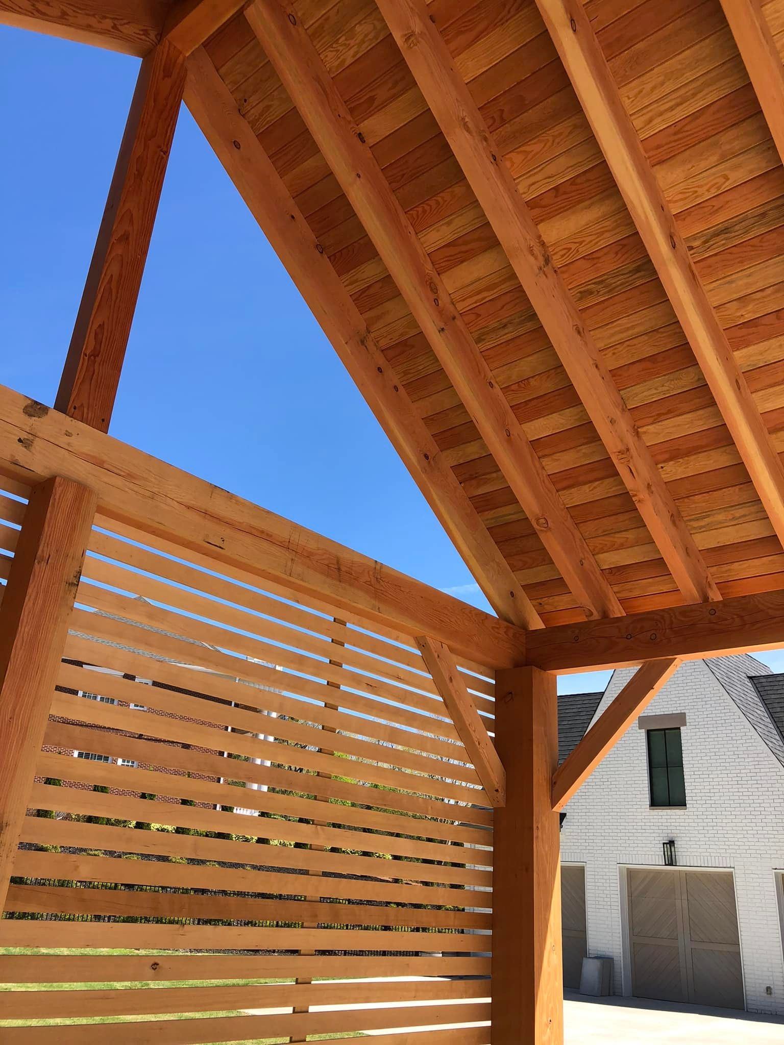 Wooden pergola with slatted side panel, blue sky visible, building in background.