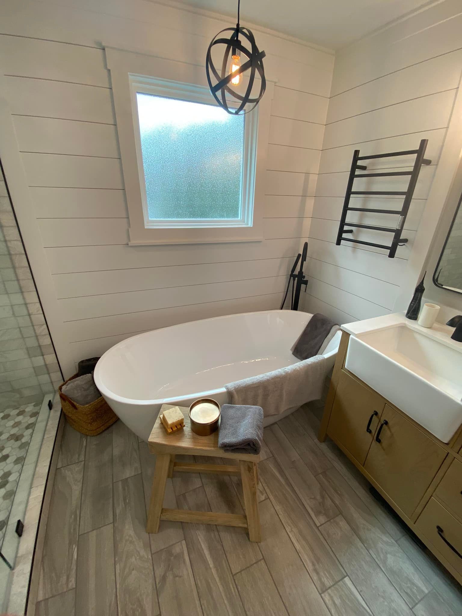 Bathroom with white bathtub, wooden vanity, and light gray shiplap walls.