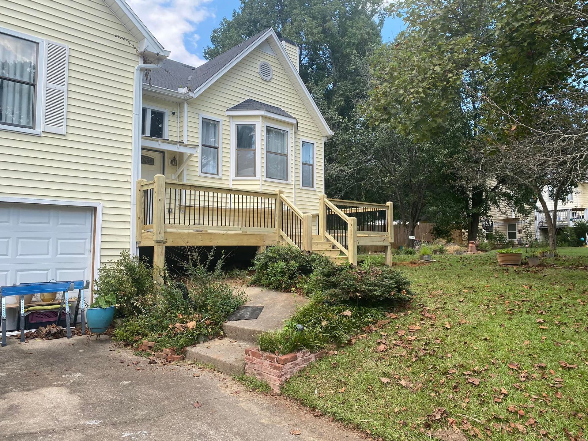 Yellow house with a newly built wooden deck, steps, and shrubs in the yard.
