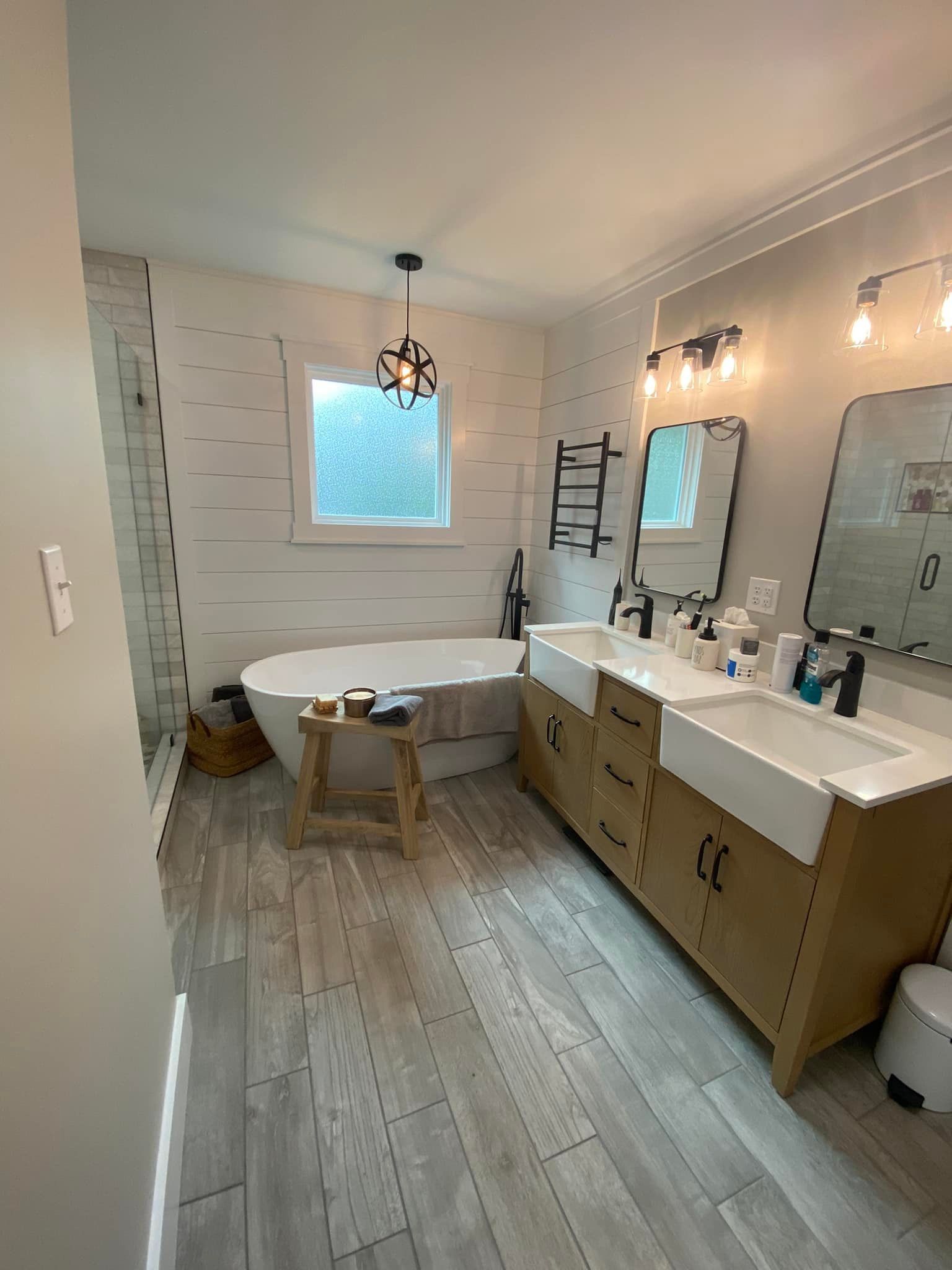 Bathroom with wood-look floors, white tub, double vanity with black fixtures, and a window.