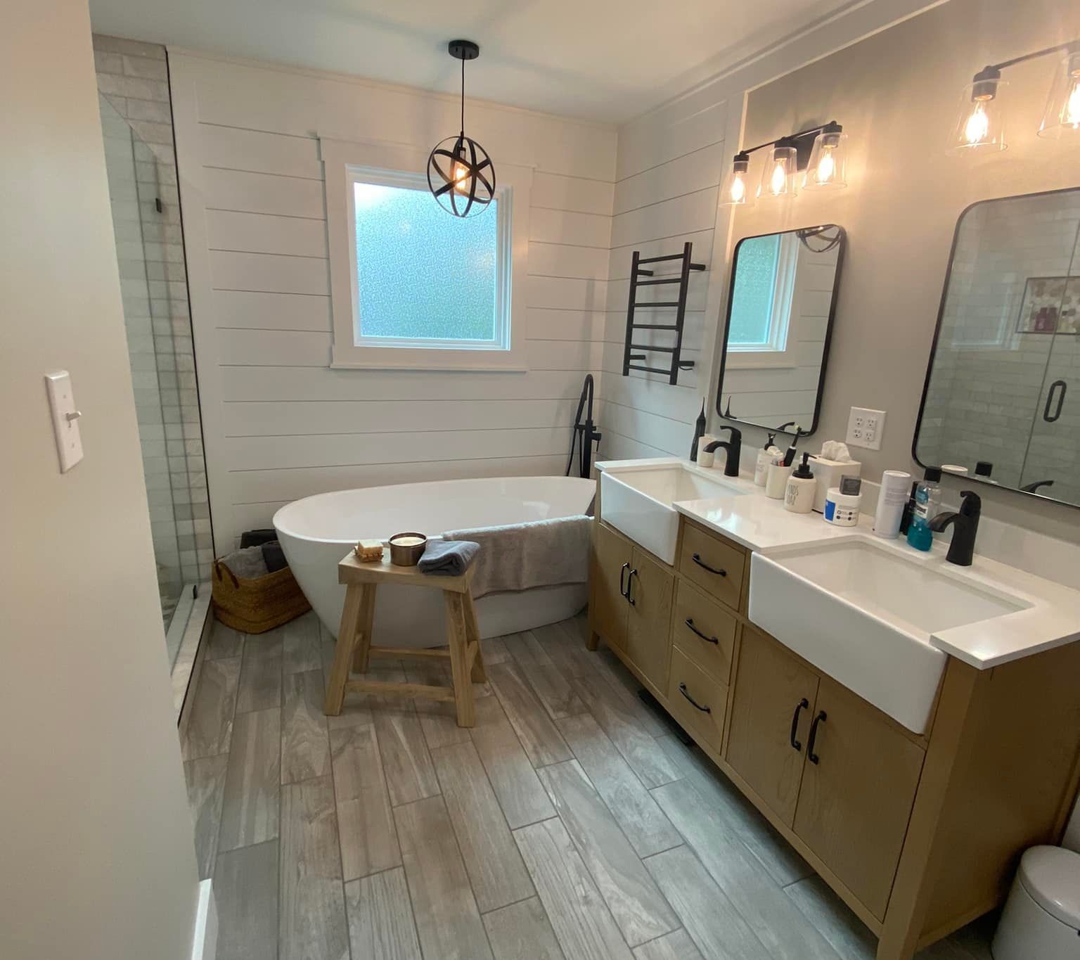 Bathroom with freestanding tub, double vanity, and gray wood-look tile floor. White shiplap walls.