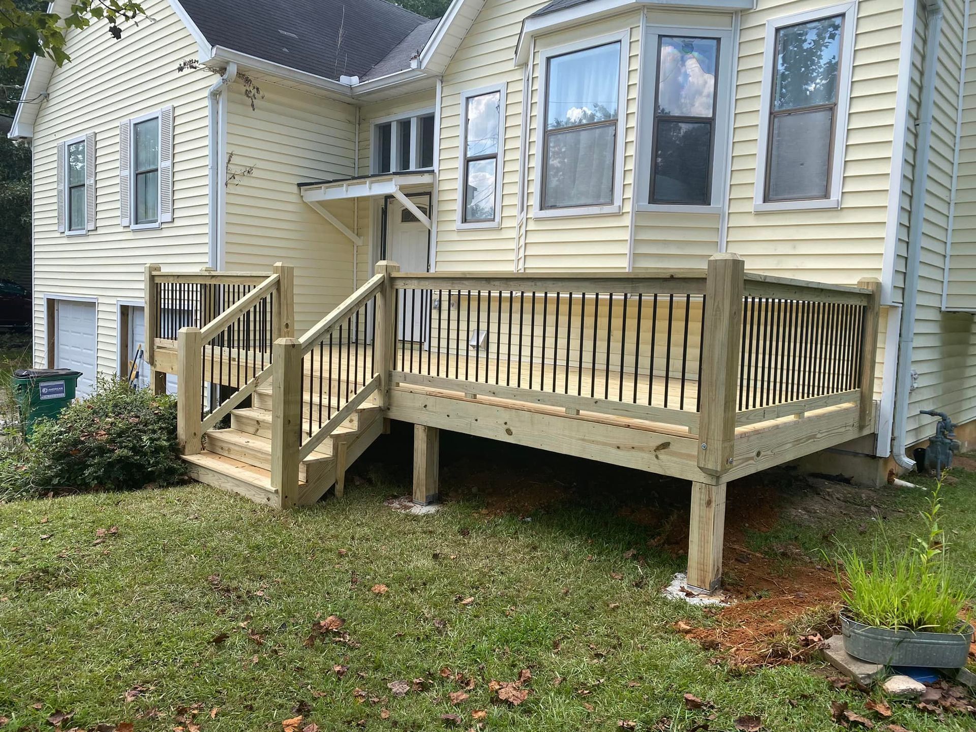 Newly built wooden deck attached to a light yellow house with dark shutters and black railing.
