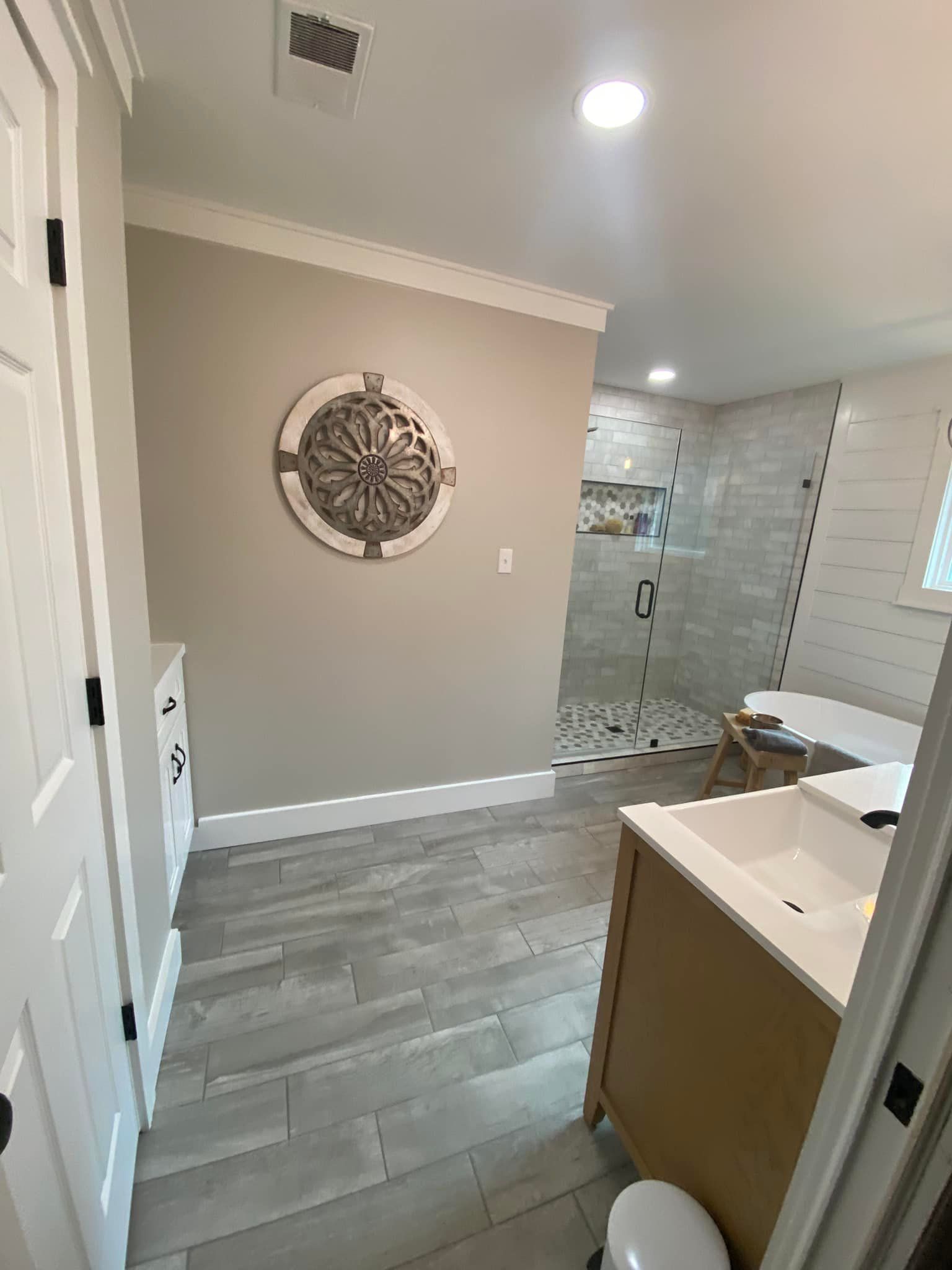Bathroom with shower, vanity, and a decorative compass on the wall. Light gray walls, flooring, and cabinetry.