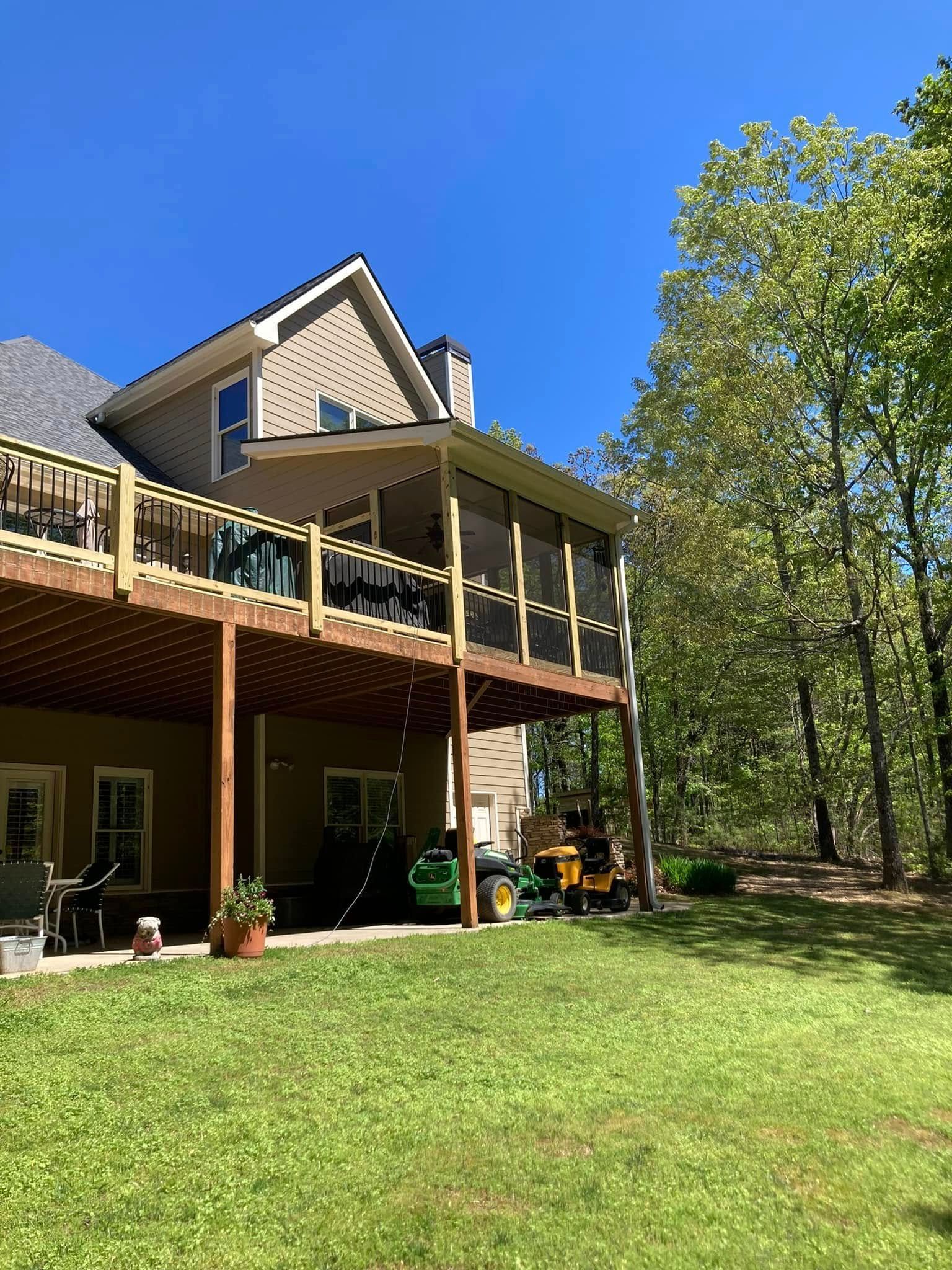 Wooden deck with a screened porch attached to a beige house, green lawn and trees.