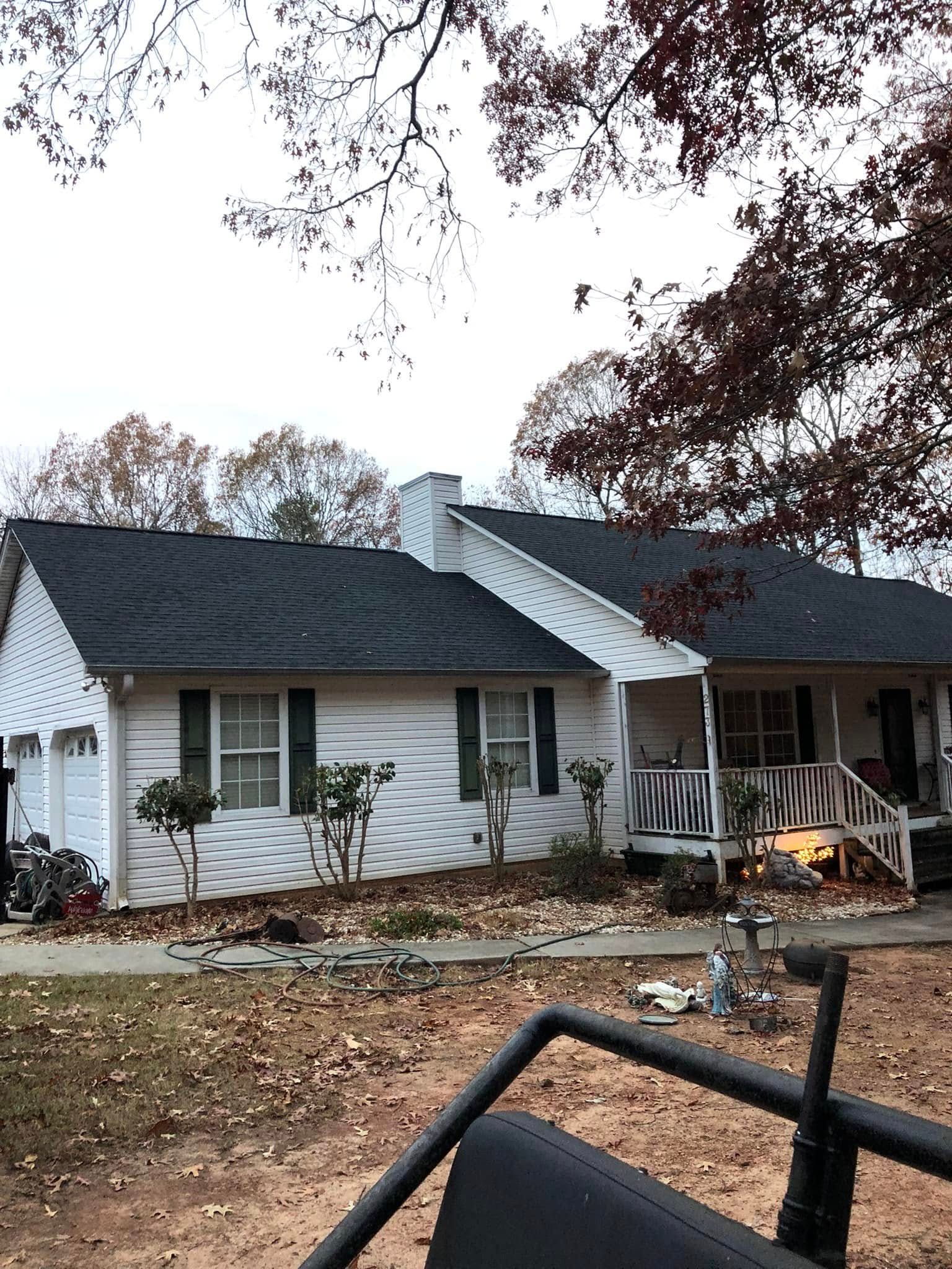 White house with black roof and chimney; porch, windows, and trees in front.