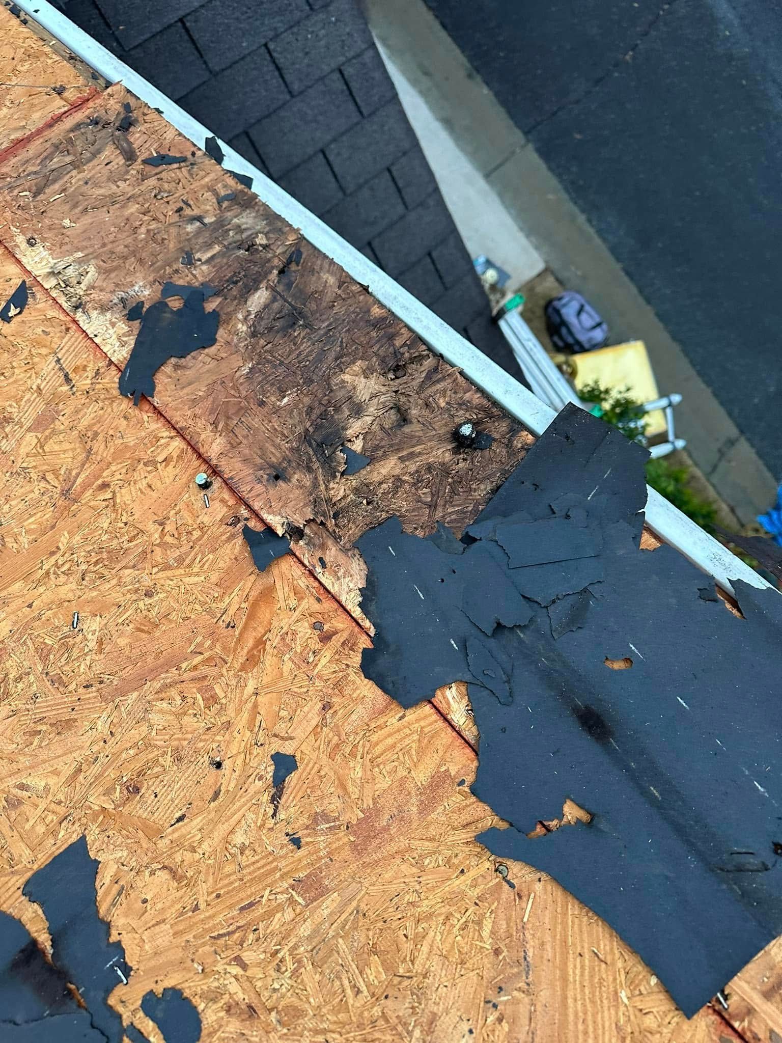 Close-up of a roof edge with exposed wood, damaged shingles, and a gutter, likely indicating roof repair.