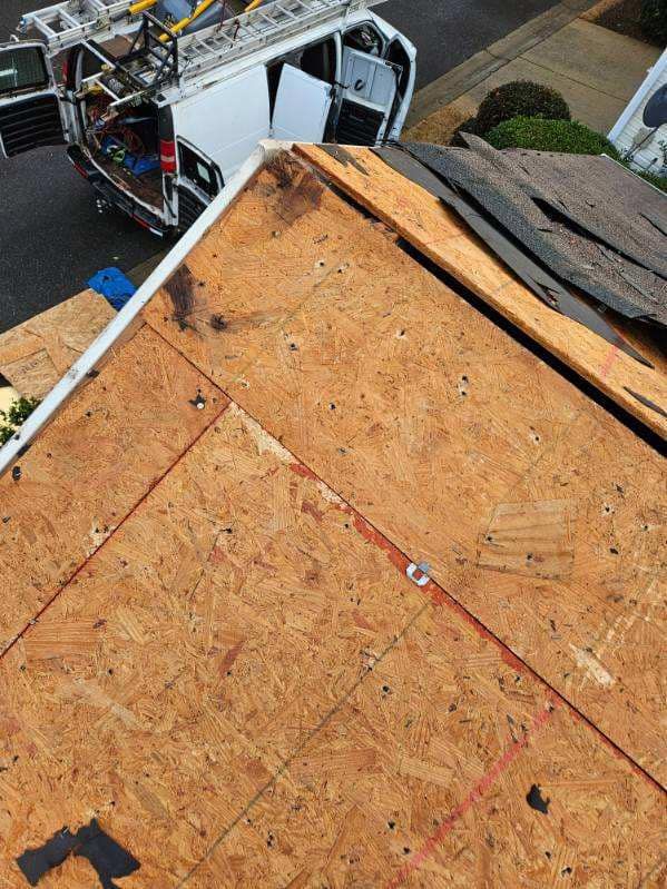 Overhead view of a roof with exposed wood panels. A white van with open doors is parked nearby.