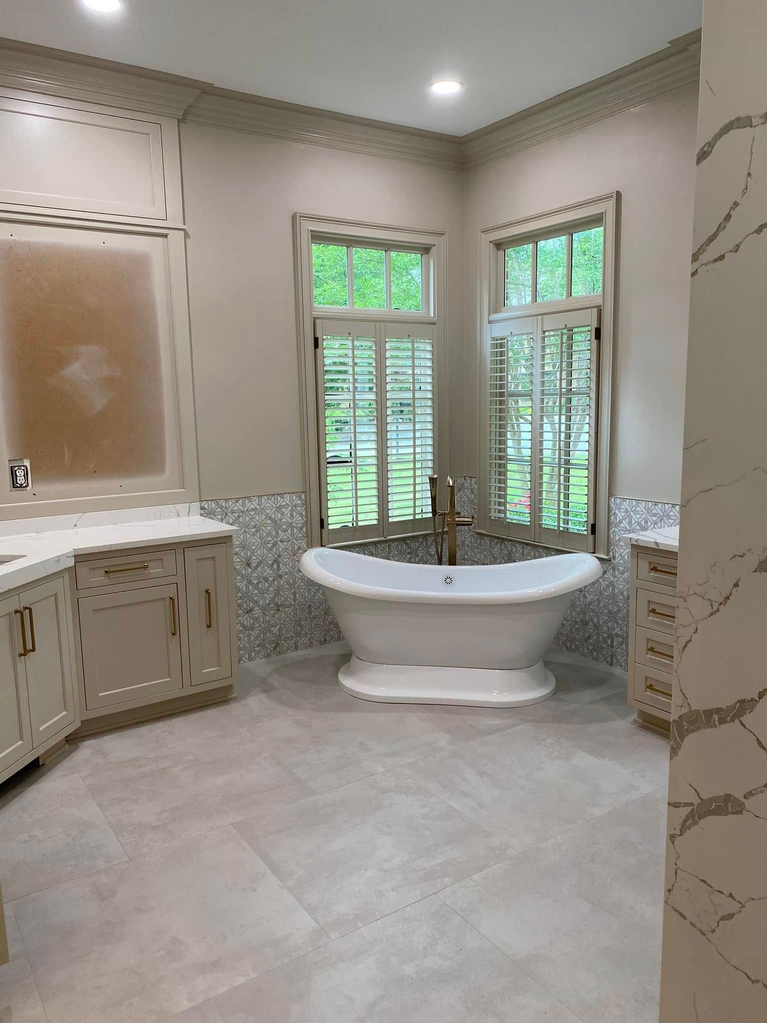Bathroom with a white clawfoot tub under a window with shutters. Beige cabinets, tile floor, and light walls.