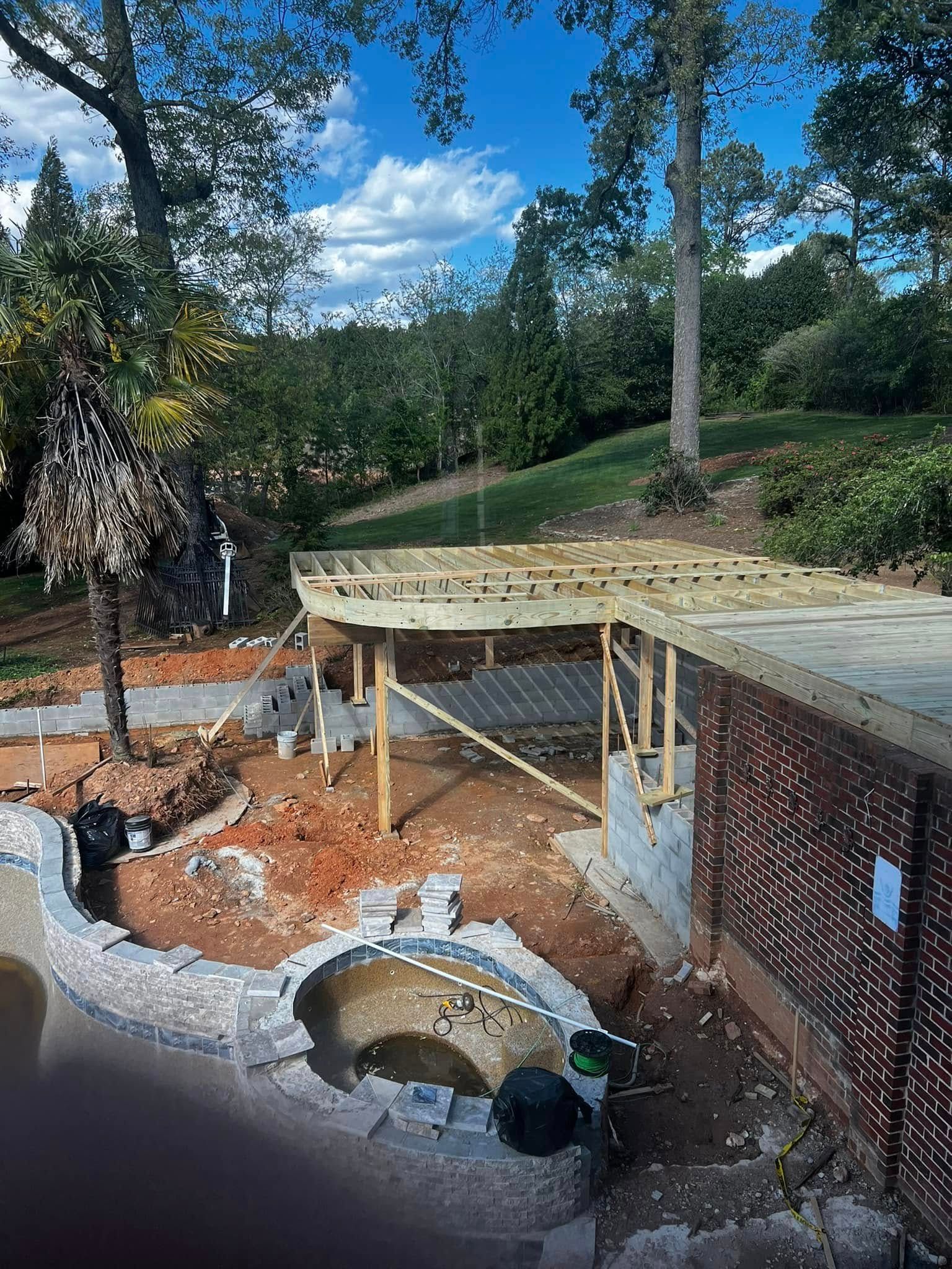 Construction of a wooden deck near a pond and hillside with blue sky.