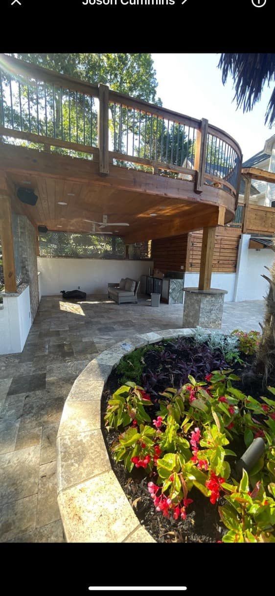 A multi-level wooden deck with stone columns and flower bed in front of a white wall.