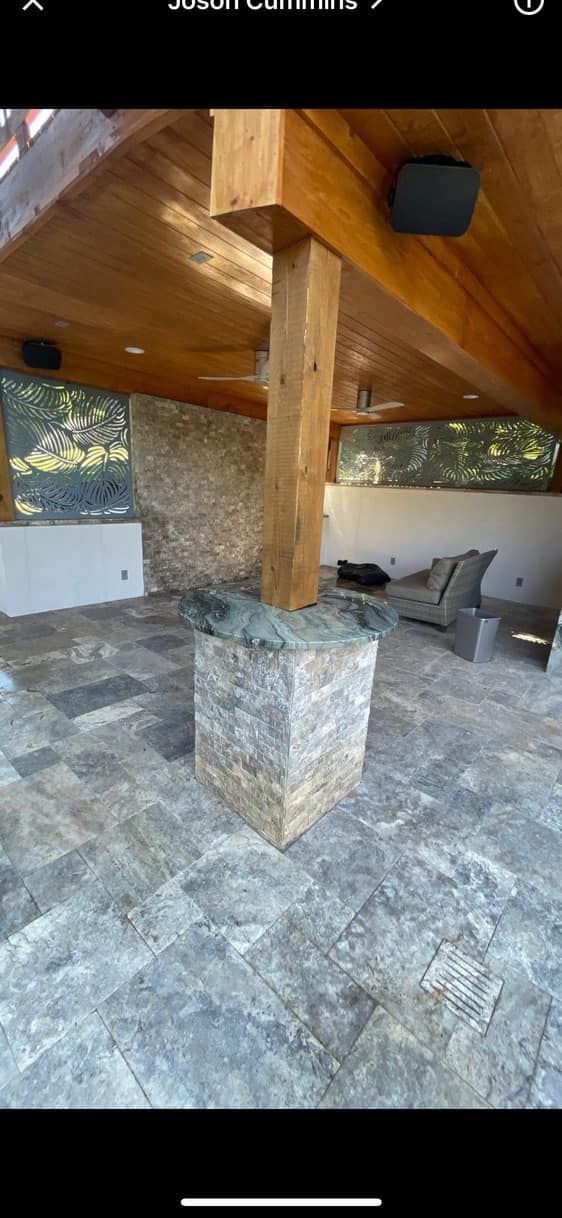 A covered outdoor patio with wood beams, stone tile, and a stone-covered support pillar.