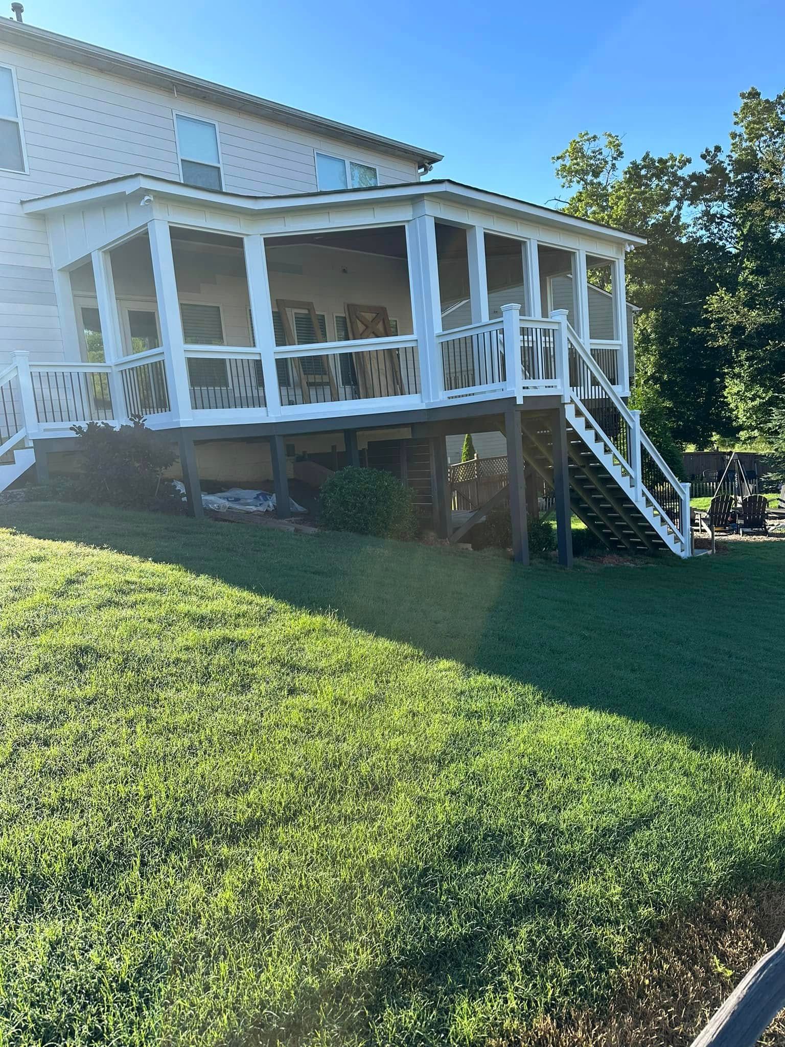 White porch with railings attached to a two-story beige house; green grass in front.