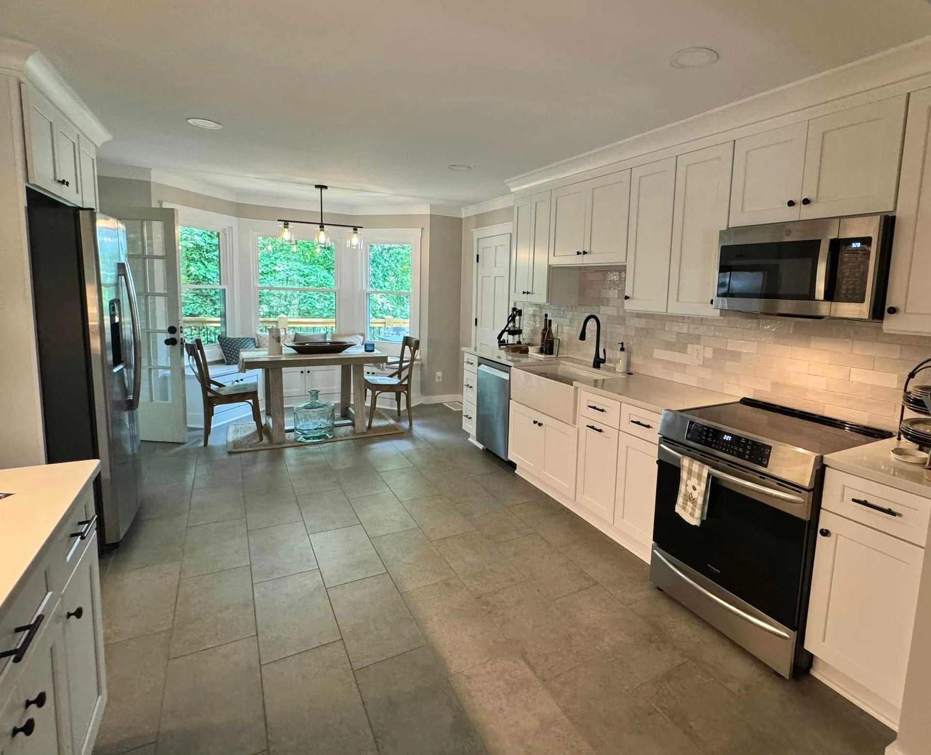 Spacious kitchen with white cabinets, stainless steel appliances, and a dining area by a window.