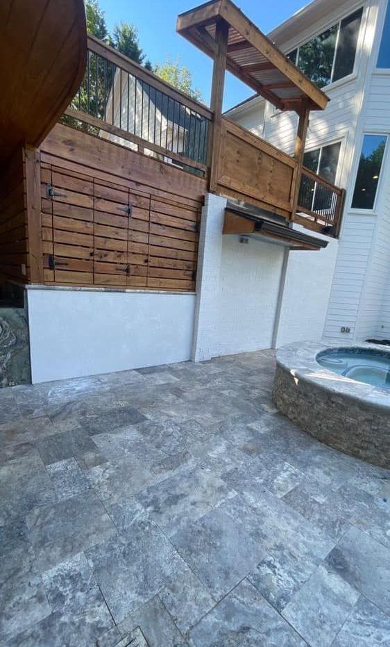 Outdoor patio with textured stone, white walls, wooden structures, and a hot tub.