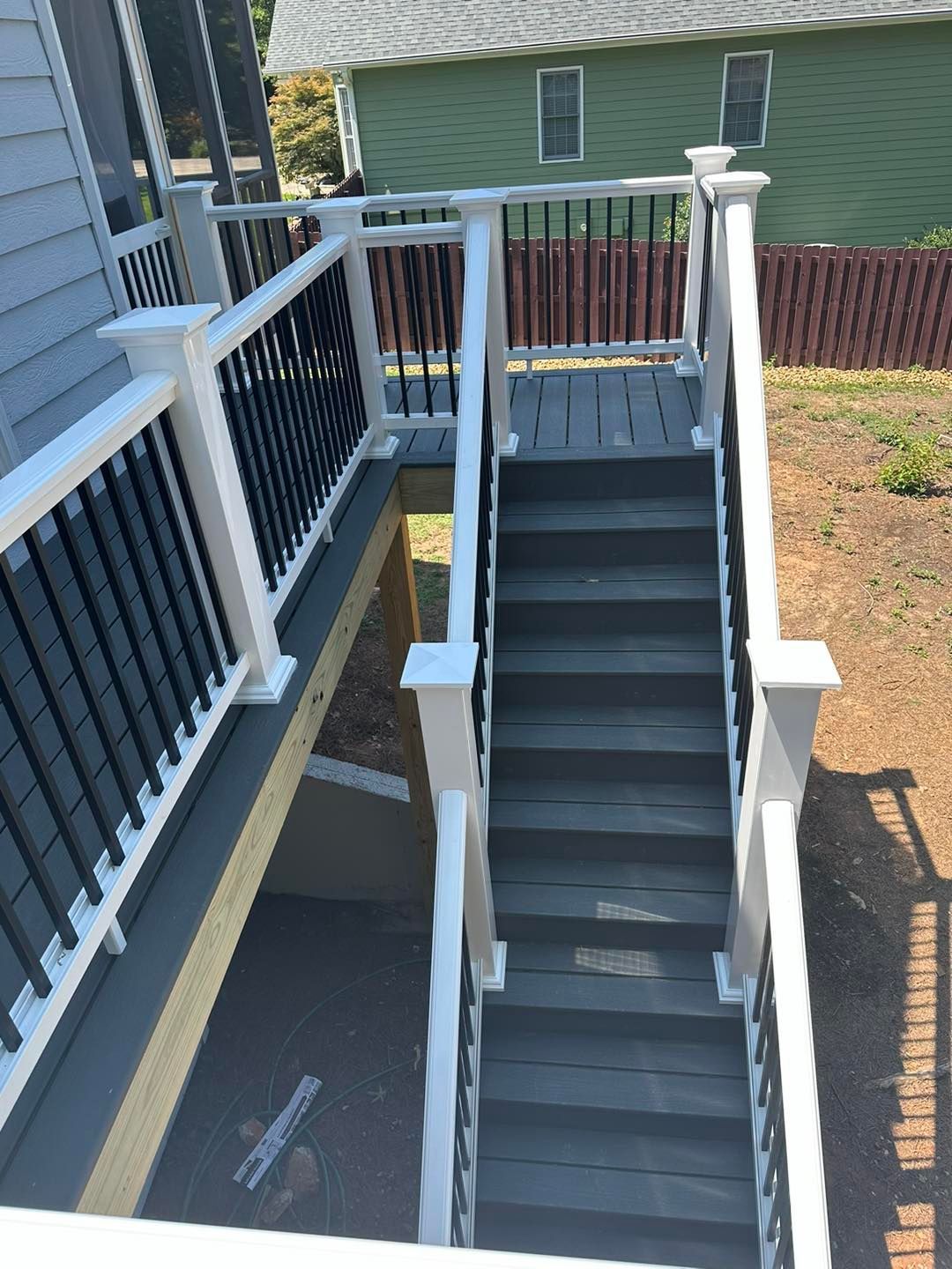 Wooden deck with stairs, black railing, and white posts leading to a house.