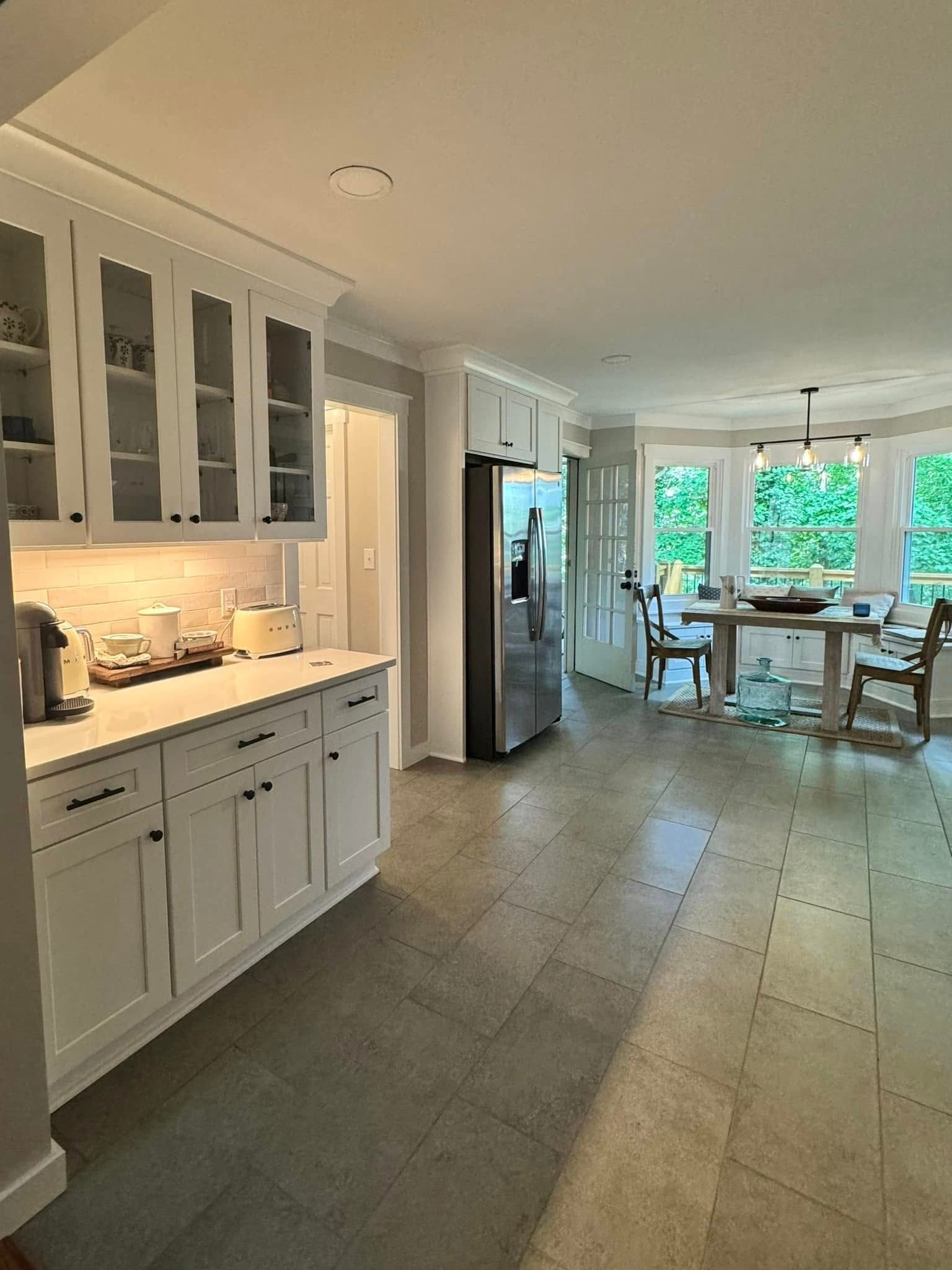 White kitchen with cabinets, stainless steel refrigerator, and dining area with a table and chairs.