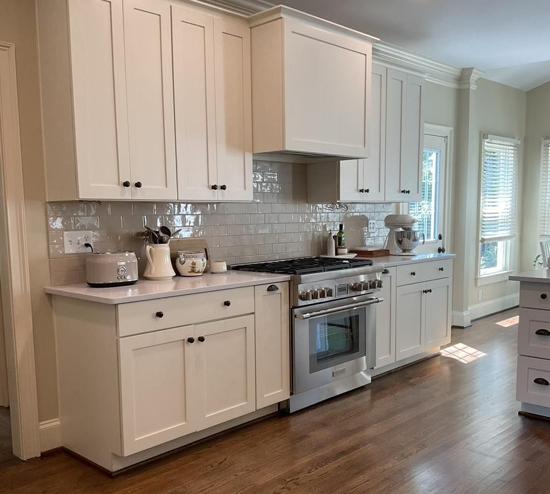 White kitchen cabinets with stainless steel range and light-colored countertops; hardwood floors.