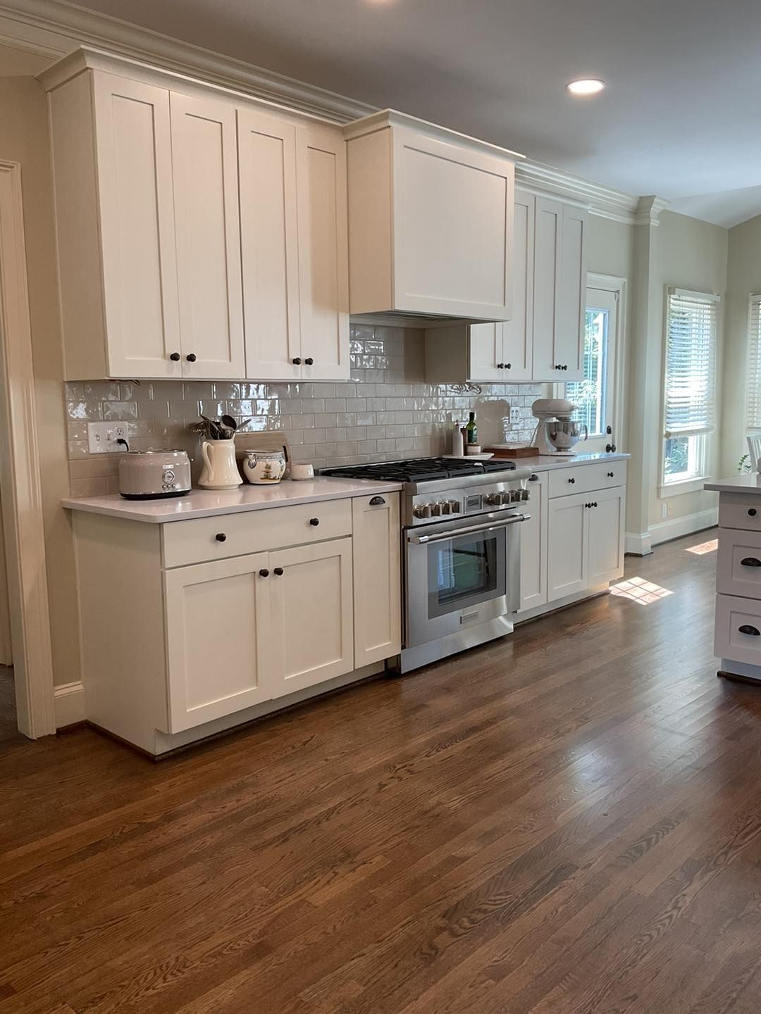 White kitchen with light wood floor, white cabinets, stainless steel stove, and white backsplash.