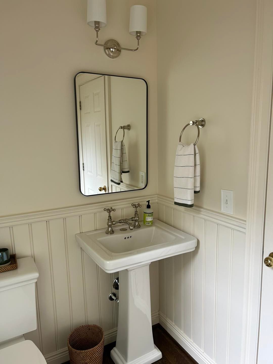 Bathroom with white pedestal sink, mirror, towel, and two-light fixture. Vertical wainscoting on walls.