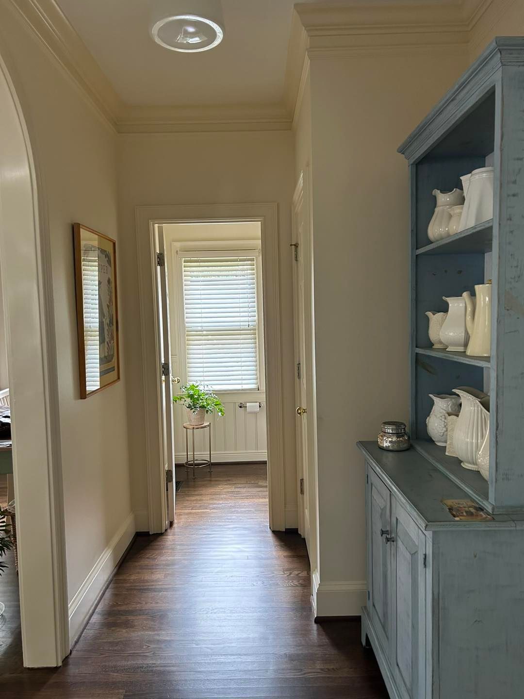 Narrow hallway with dark wood floor, light walls, and blue cabinet with white dishware.