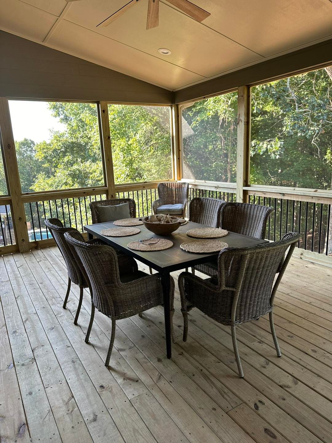 Screened-in porch with a square dining table, surrounded by wicker chairs, overlooking a wooded view.