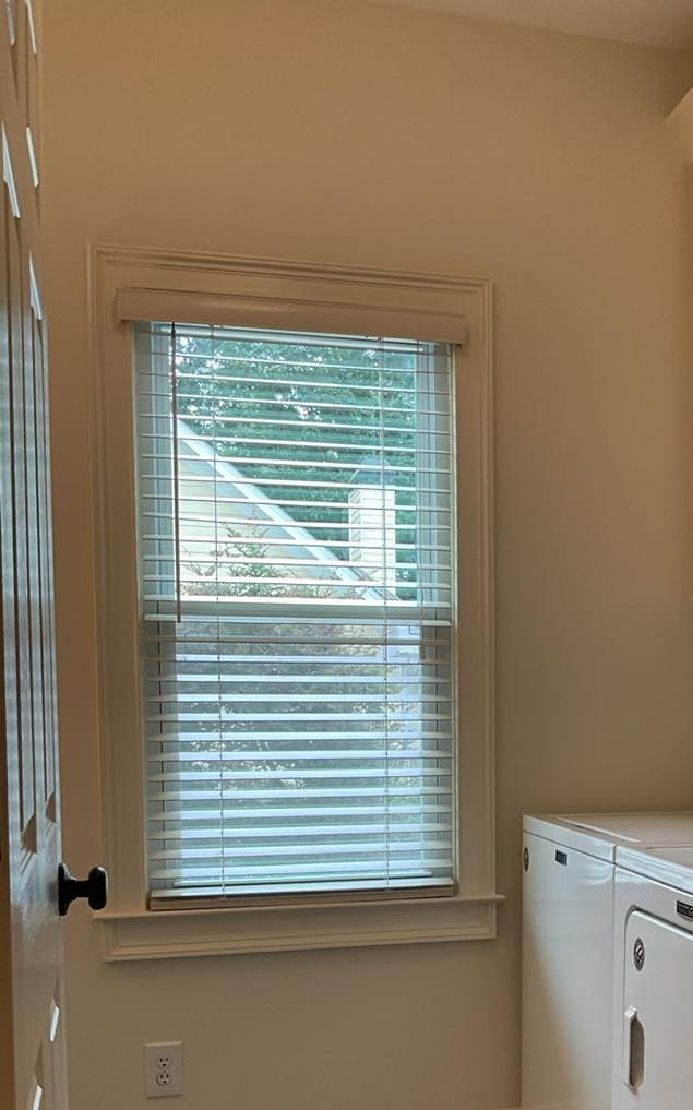 Window with blinds, looking out onto a house, in a room with a washing machine and door.