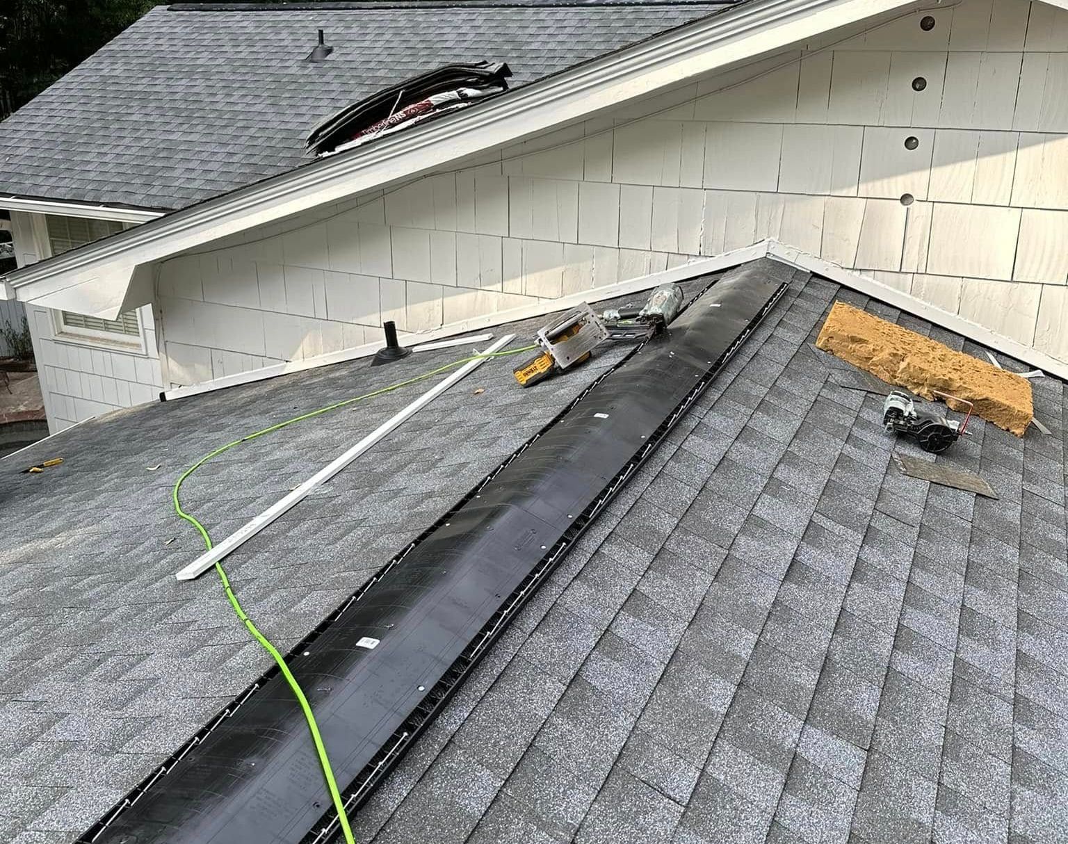 Roof under construction: dark trough, tools, shingles, and exposed sheathing visible.