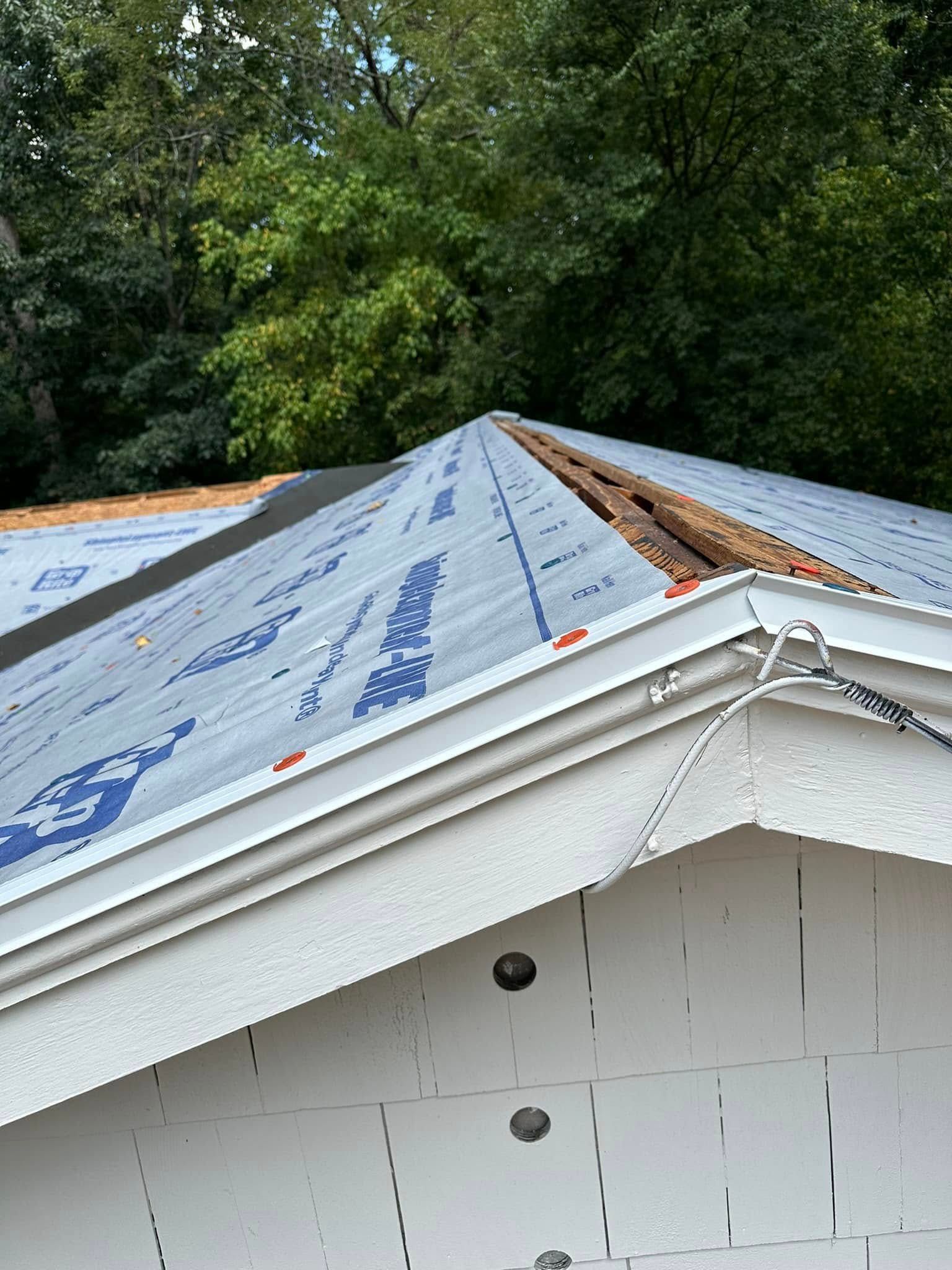Roof partially covered with blue underlayment; trees in background.