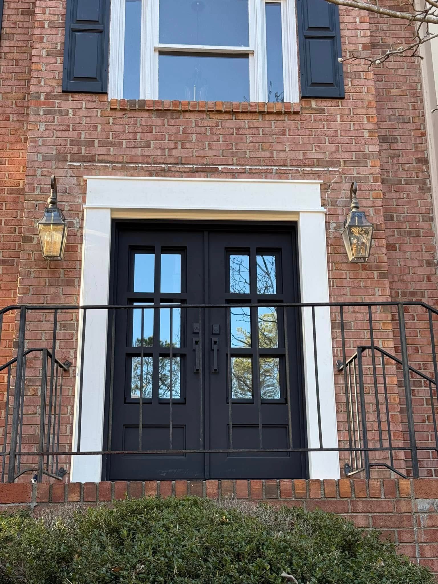 Black double front doors on a brick house with white trim, flanked by lanterns and a black railing.