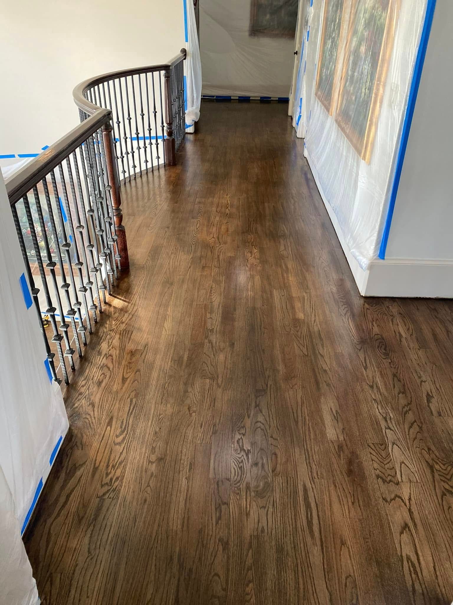 Dark wood floor hallway with a staircase to the left, and art on the wall to the right.