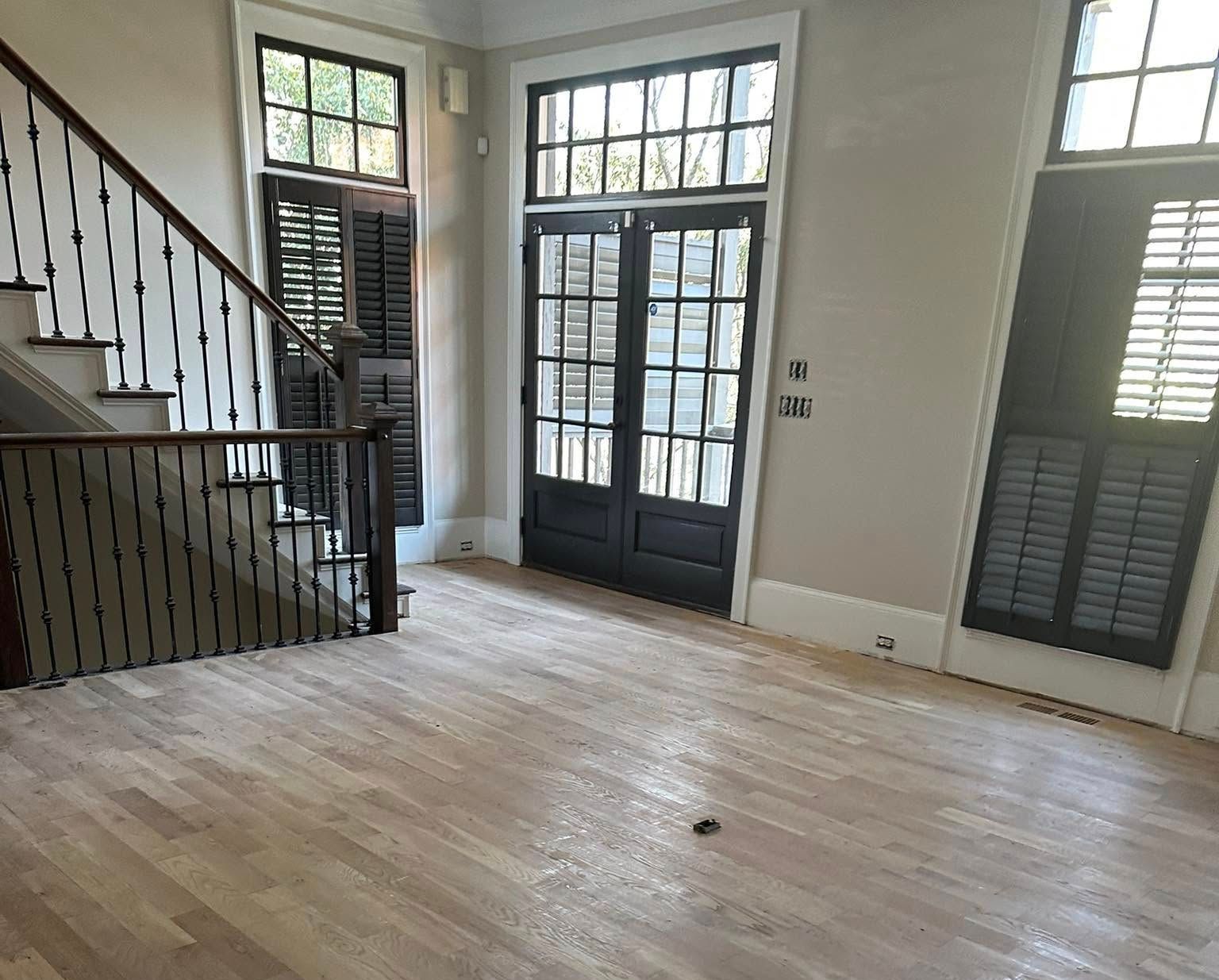 Empty room with hardwood floors, staircase, and french doors with shutters.