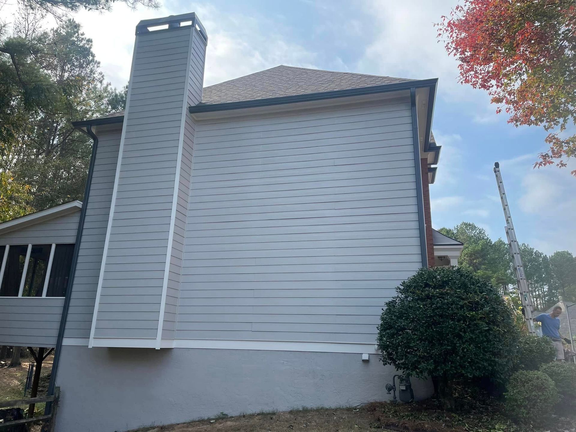 Side view of a house with light gray siding, chimney, and a small porch on a partly sunny day.