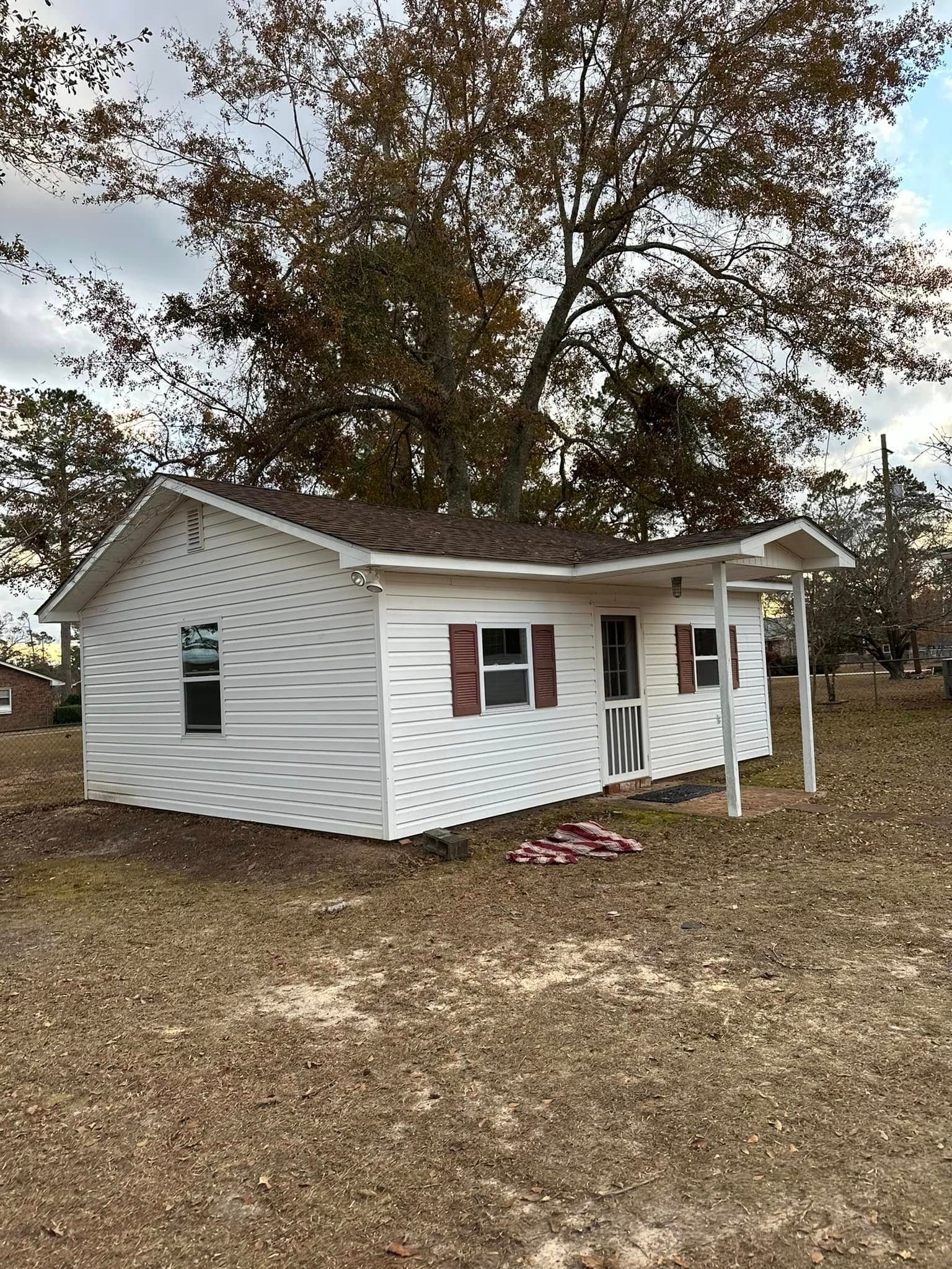 White house with brown roof, red shutters, and small porch under a cloudy sky.