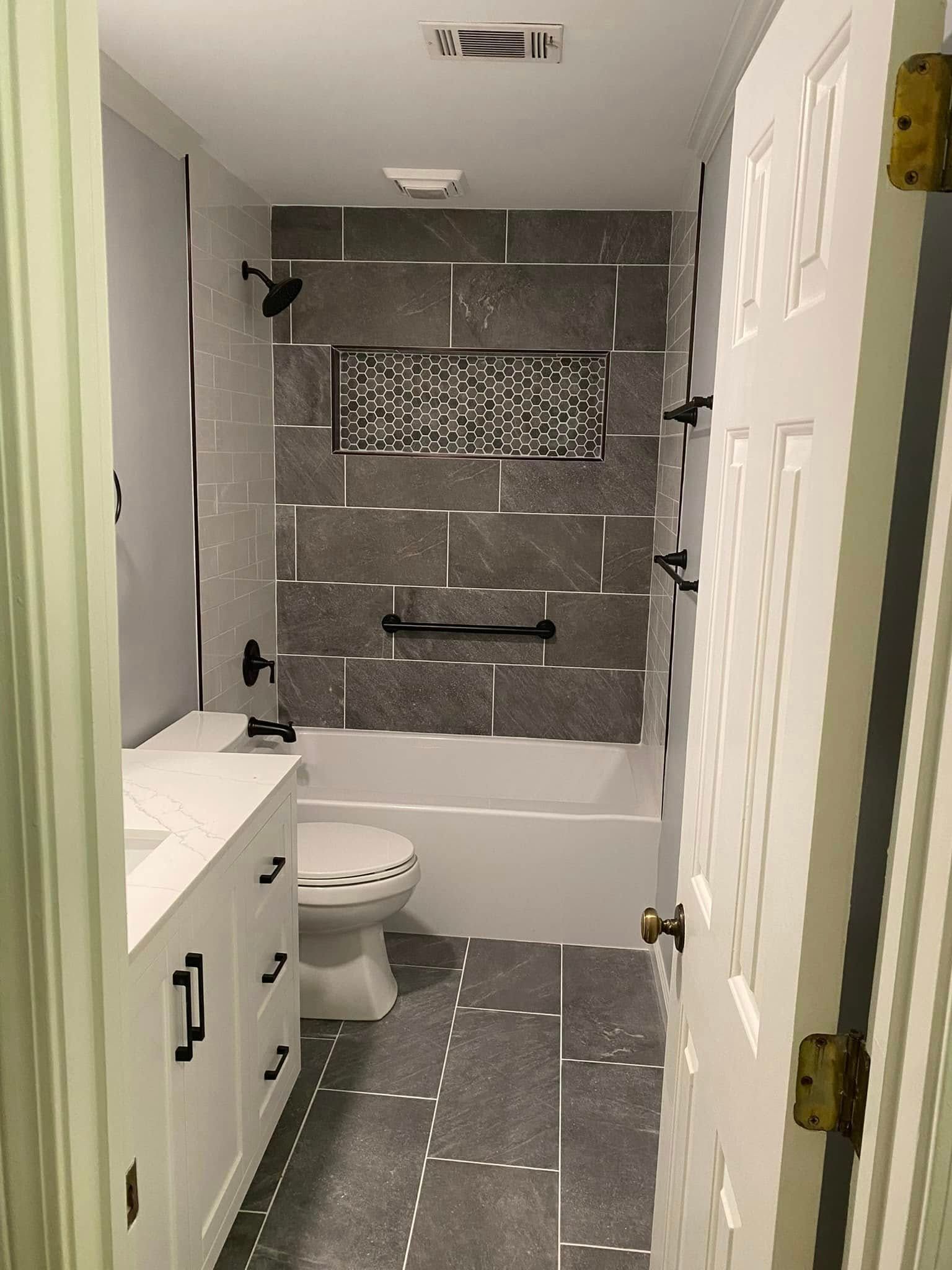 Bathroom with white vanity, gray tile, black fixtures, and open white door.