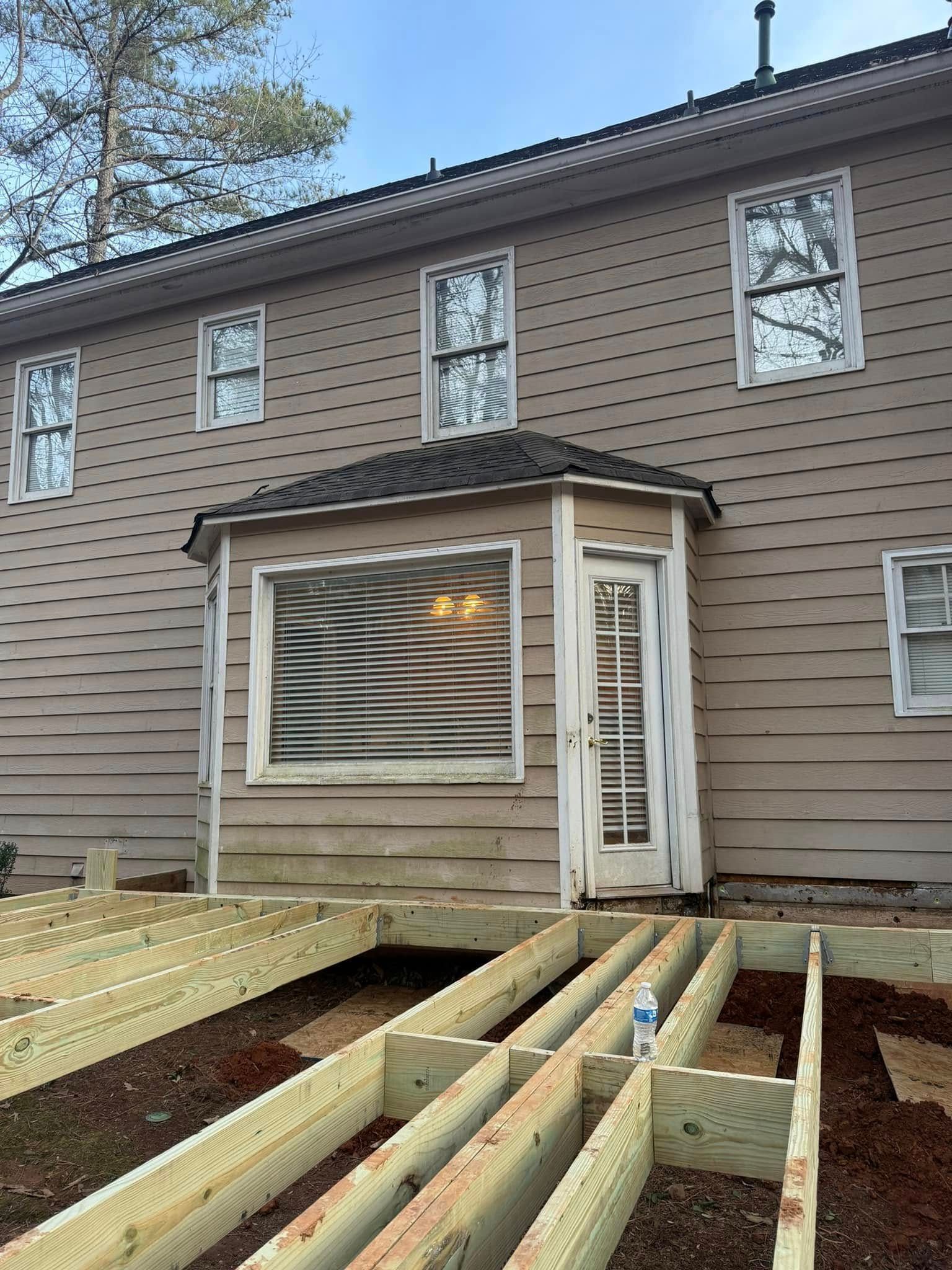 Back of a house with deck under construction. Beige siding, white-trimmed windows, and doorway.
