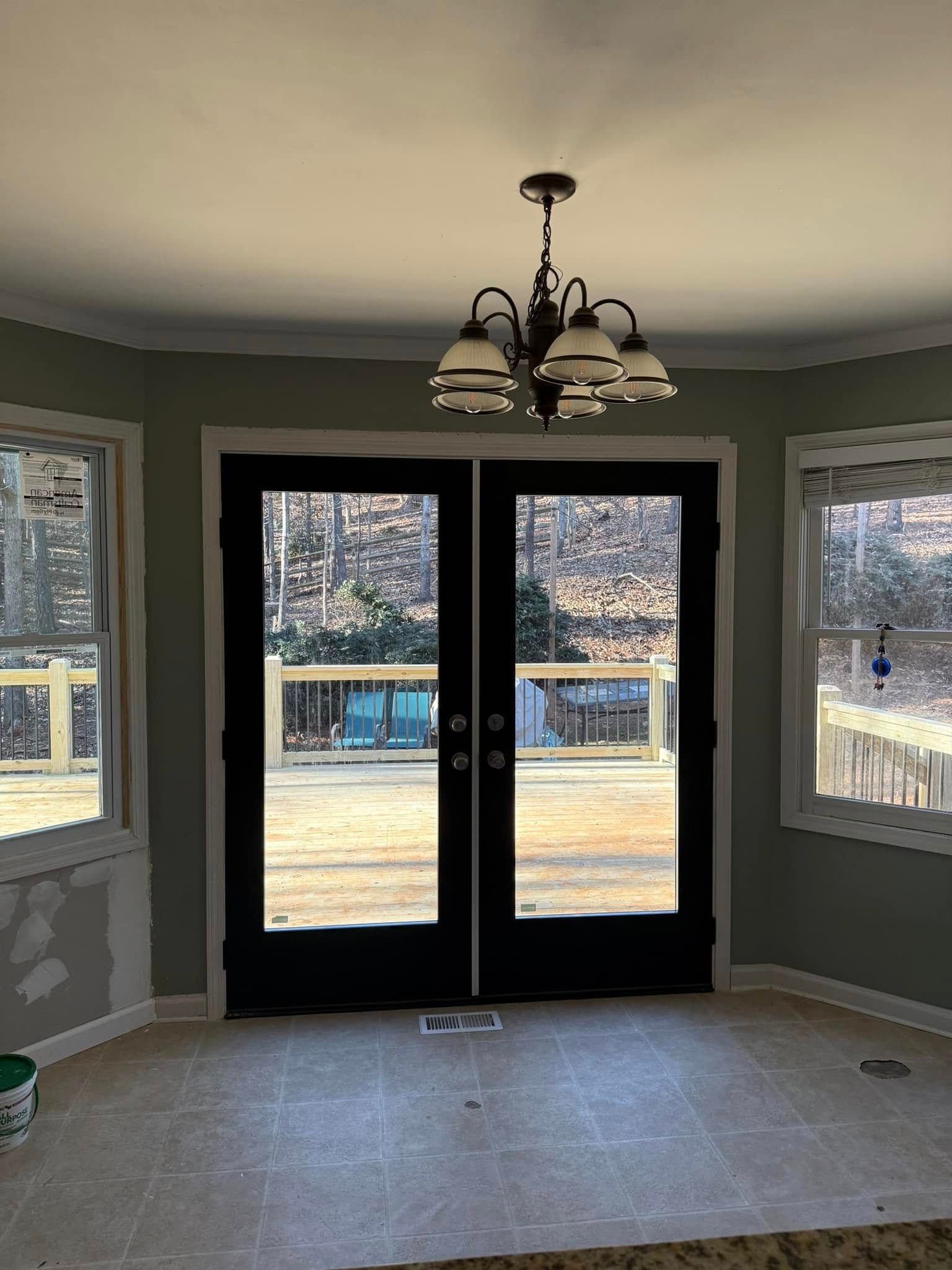 Interior view of room with black framed double doors and chandelier. Light green walls, two windows, and beige floor.