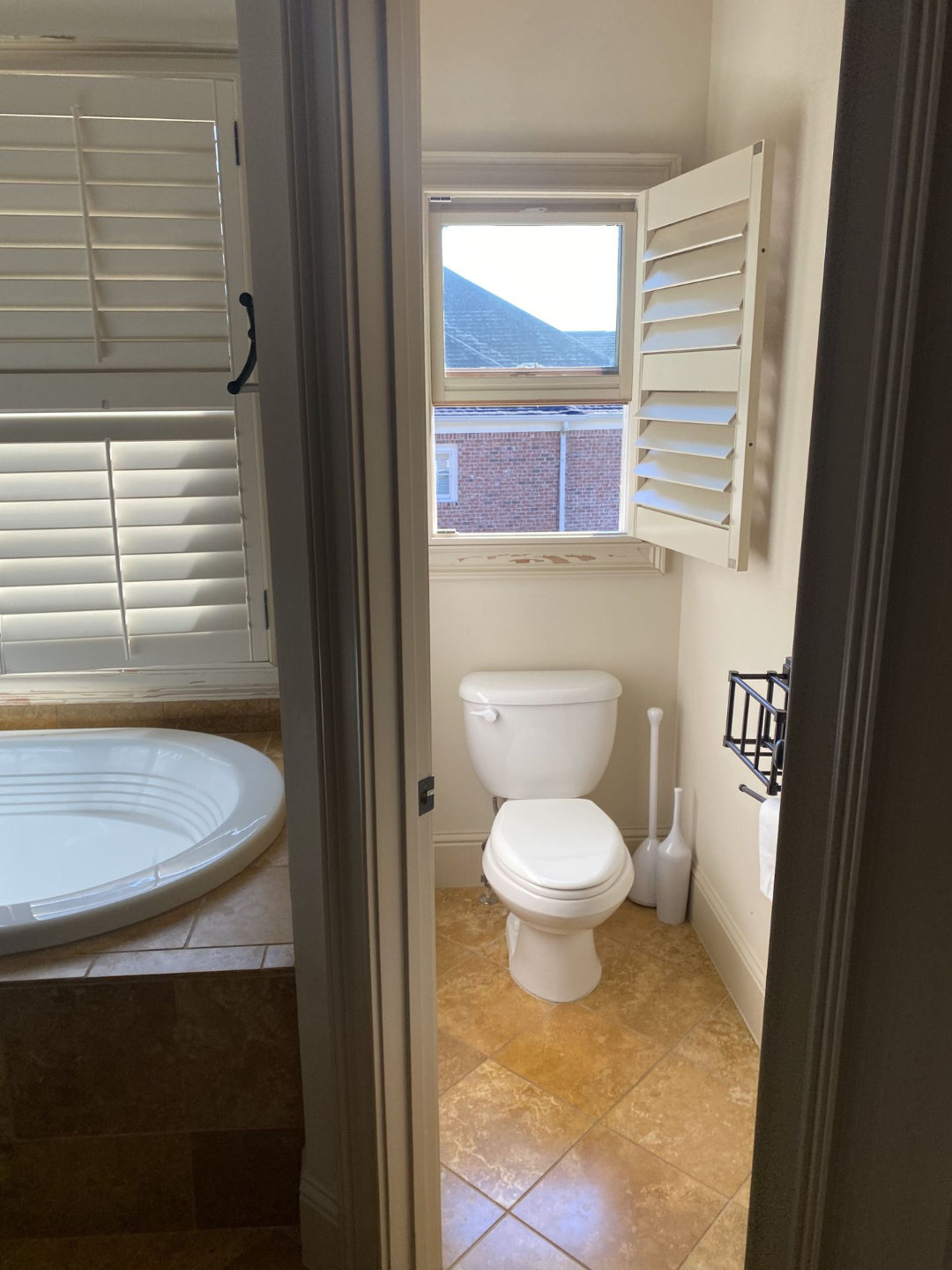 Bathroom with toilet and open shuttered window. Tub is visible to the left.