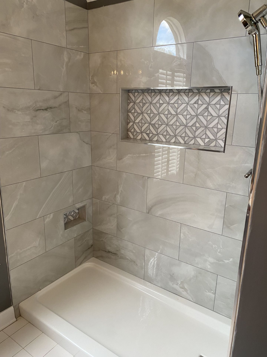 Shower stall with gray and white tile, a patterned niche, and a white shower pan.