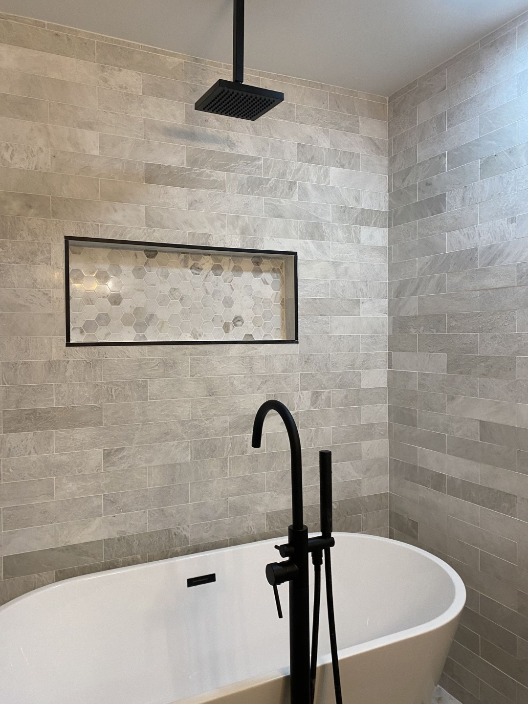 Modern bathroom with white tub, black faucet and shower, and gray tiled walls.